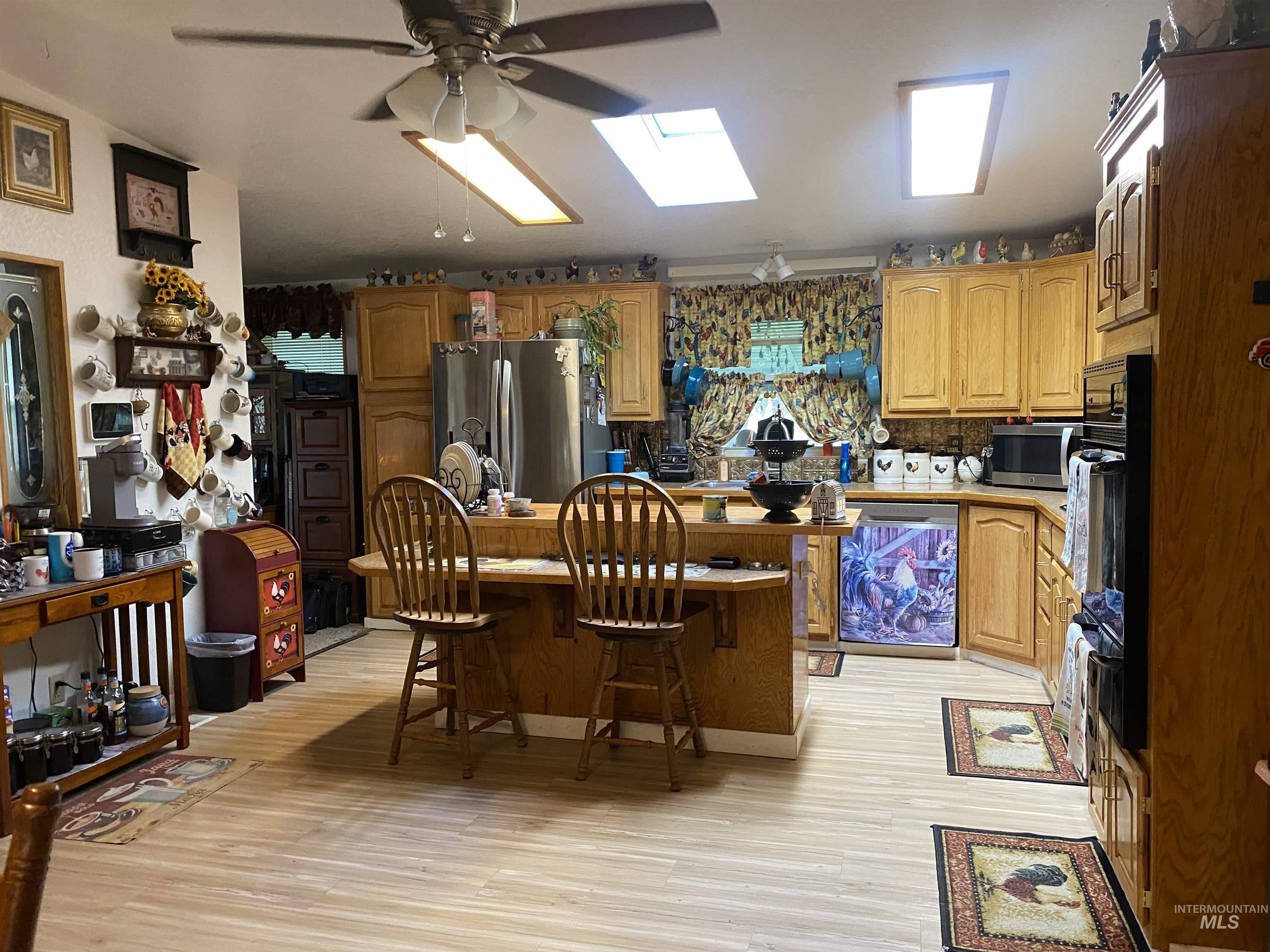 Kitchen with a kitchen bar, a kitchen island, appliances with stainless steel finishes, a skylight, and light wood-style floors