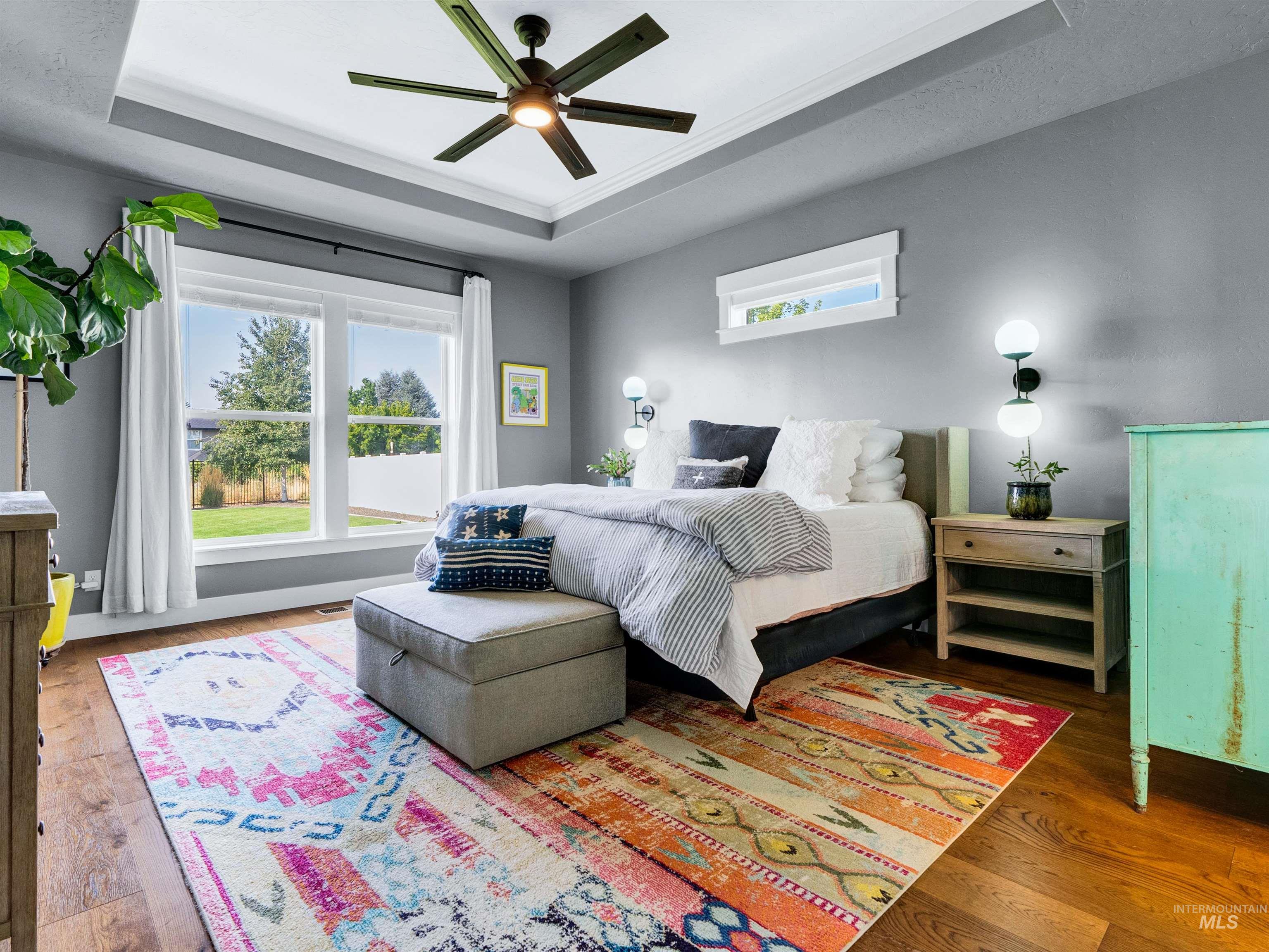 Bedroom with a raised ceiling, wood finished floors, and a ceiling fan