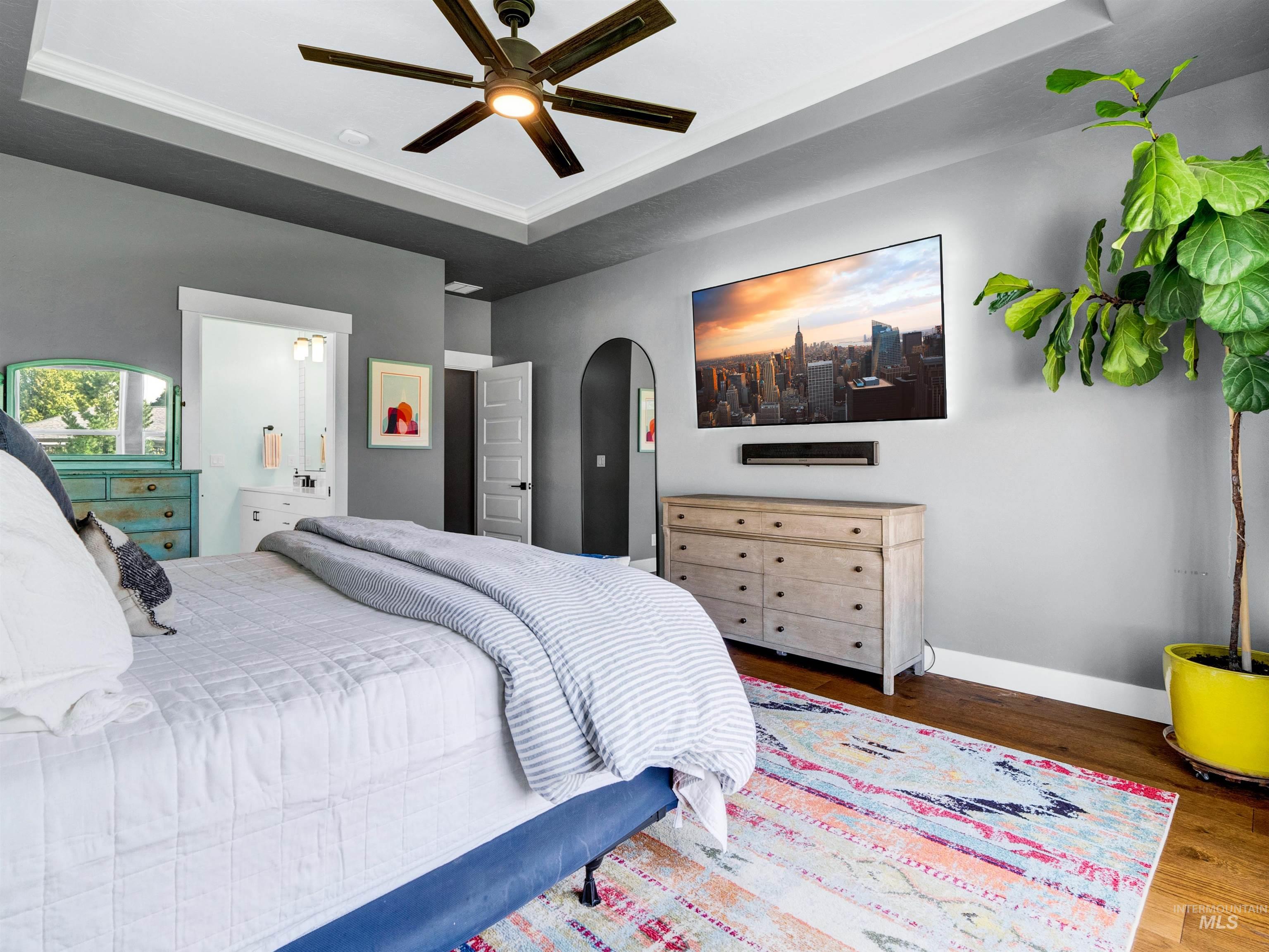 Bedroom featuring a raised ceiling, wood finished floors, arched walkways, a ceiling fan, and crown molding