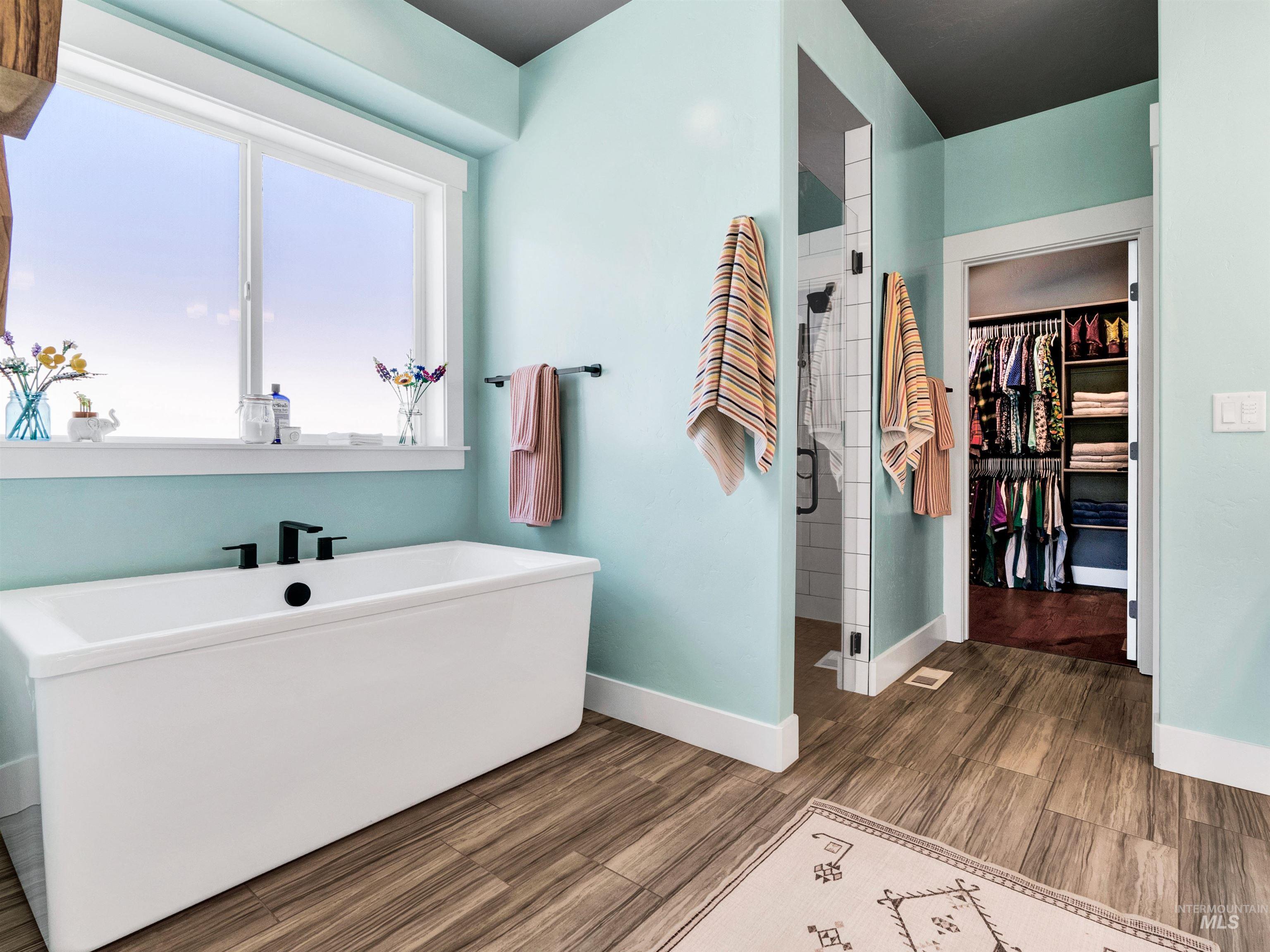 Full bathroom with a walk in closet, a shower stall, a soaking tub, and dark wood-type flooring