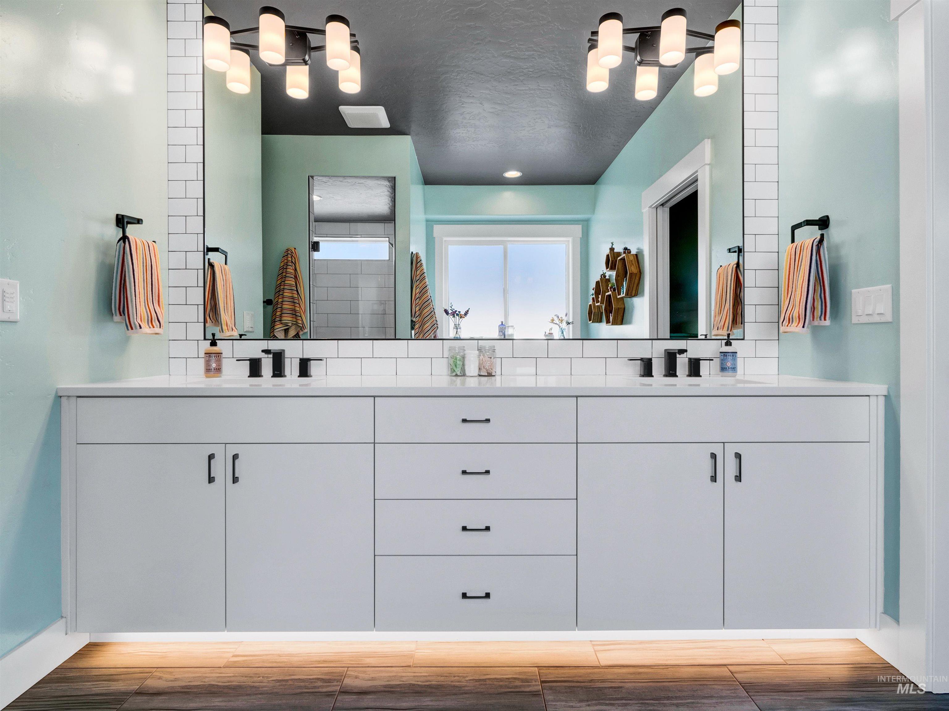 Full bath with double vanity, light wood-style flooring, and decorative backsplash