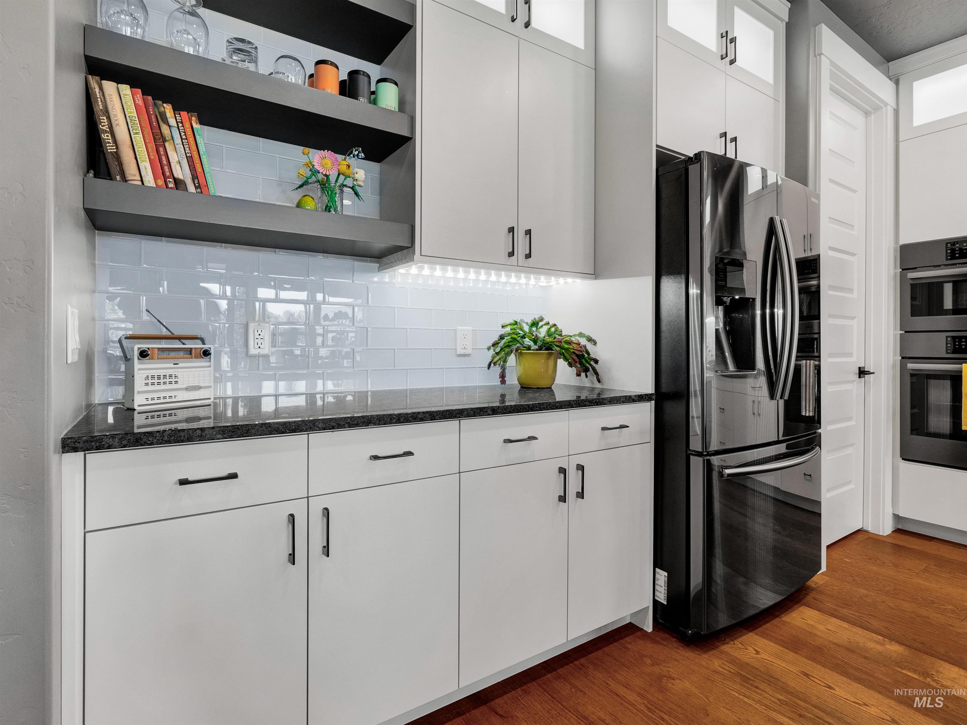 Kitchen featuring white cabinetry, dark wood-style flooring, stainless steel appliances, open shelves, and dark stone counters