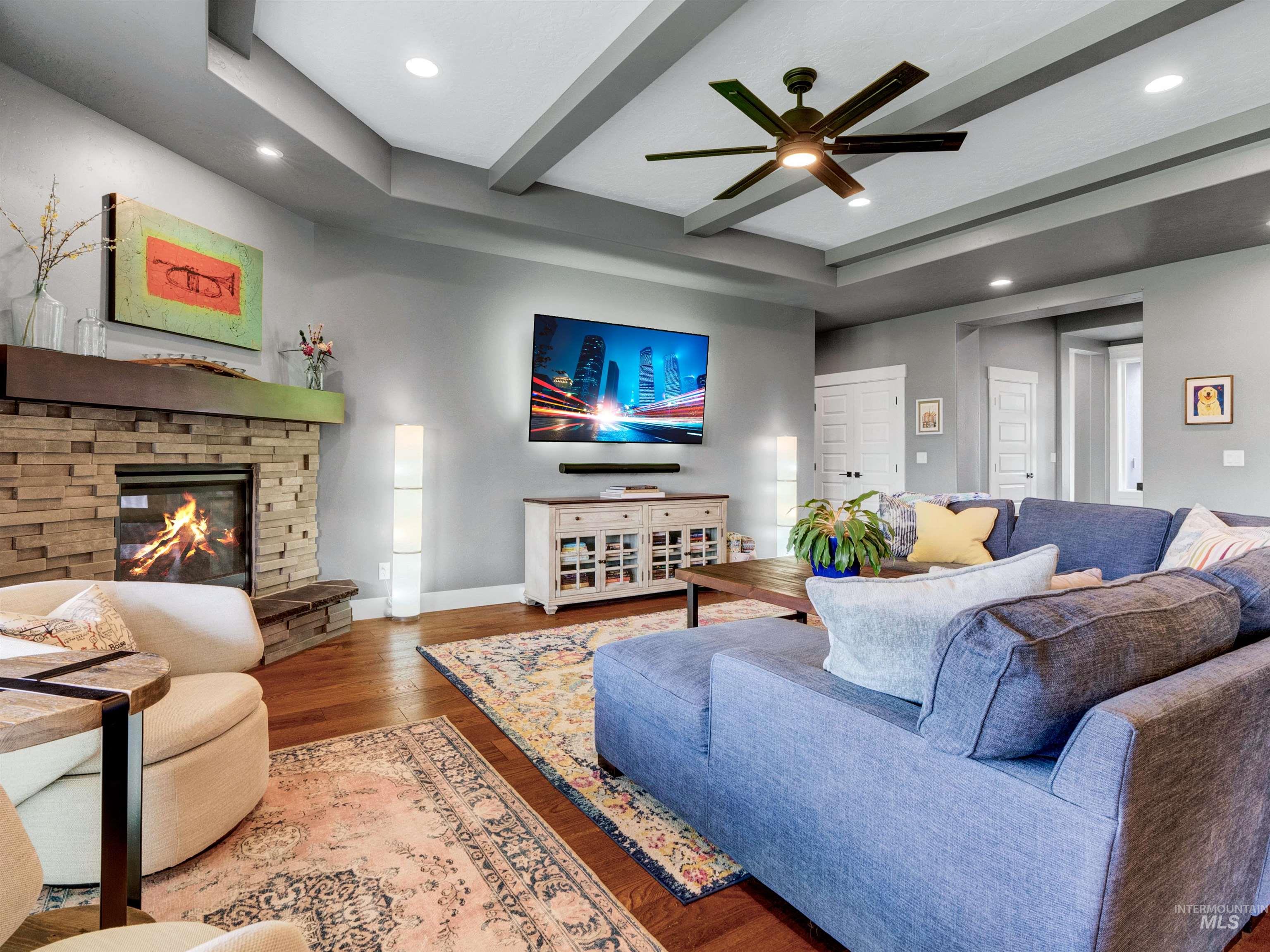 Living room with beam ceiling, wood finished floors, a stone fireplace, a ceiling fan, and recessed lighting