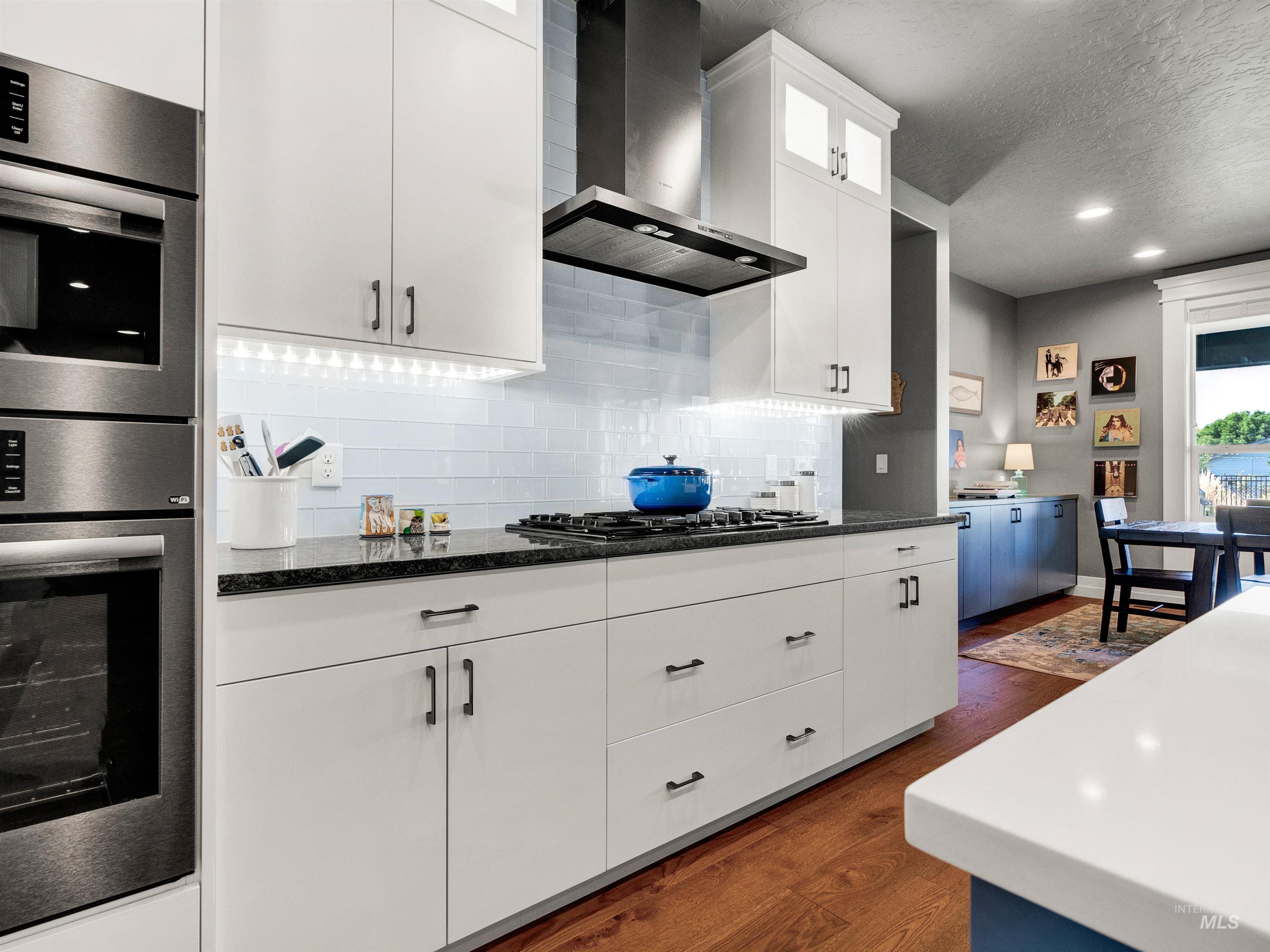 Kitchen with stainless steel double oven, wall chimney exhaust hood, white cabinets, dark wood-style floors, and a textured ceiling