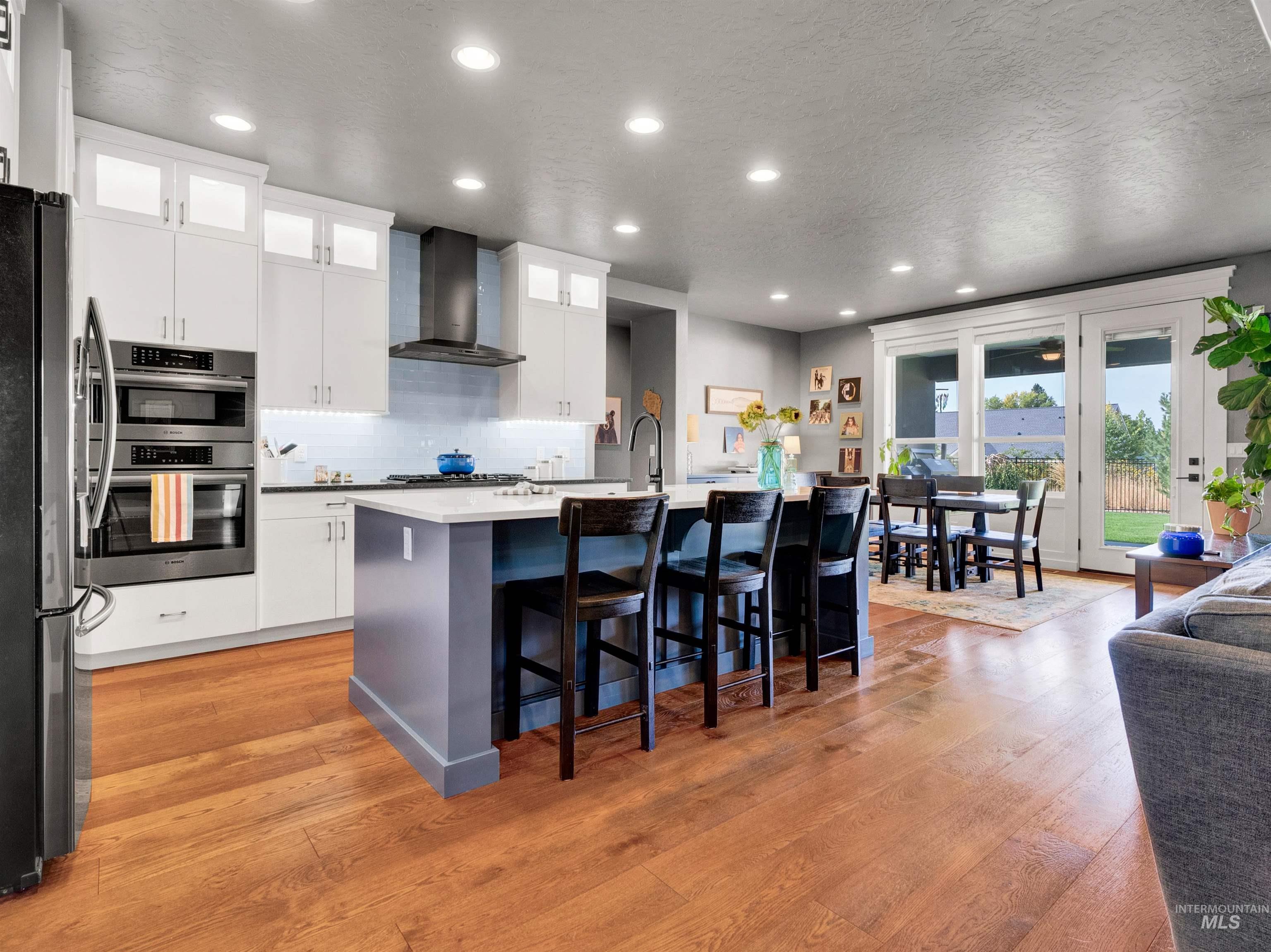Kitchen featuring white cabinets, a breakfast bar, glass insert cabinets, recessed lighting, and wall chimney exhaust hood