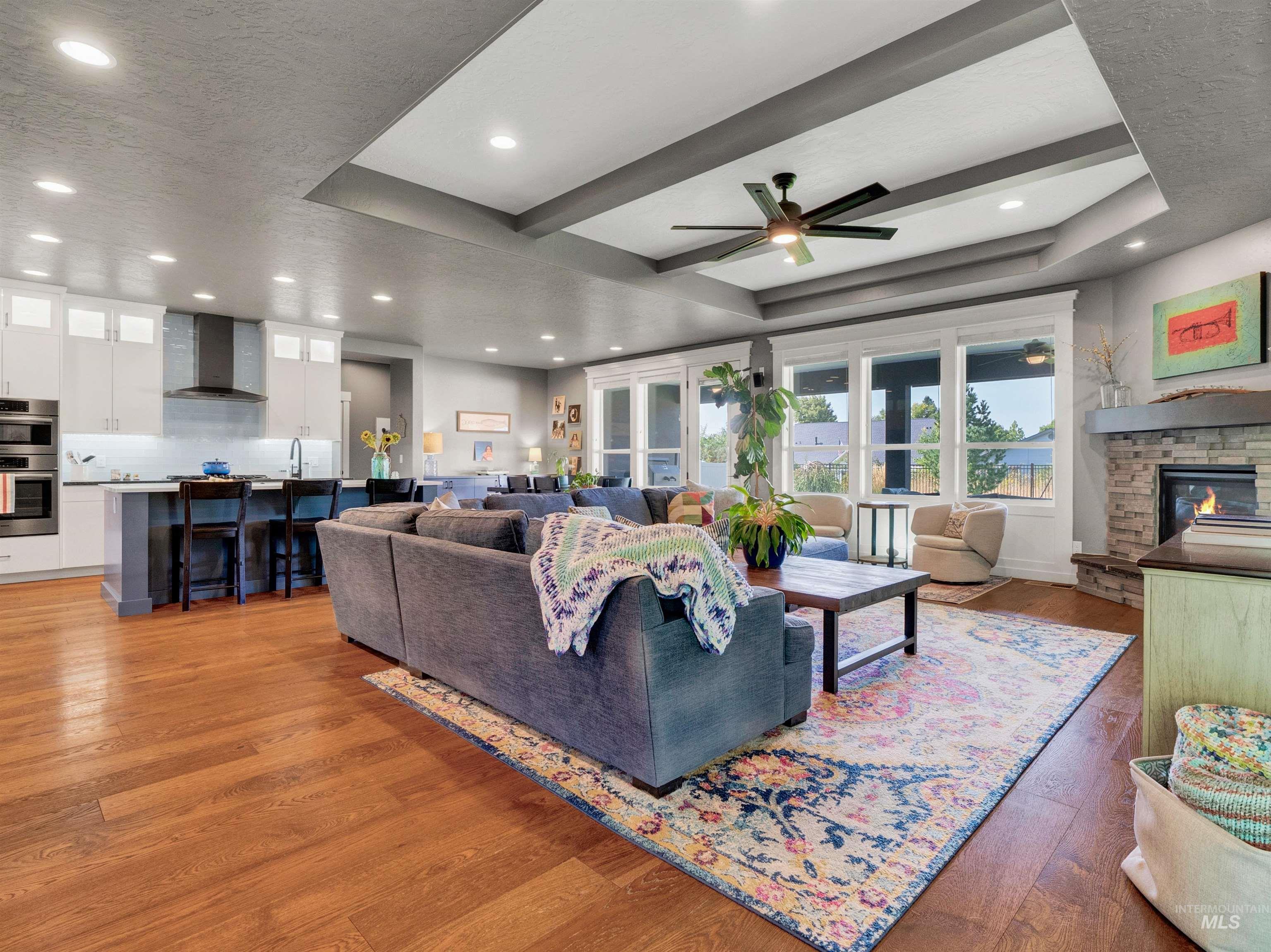 Living room featuring light wood-style flooring, a raised ceiling, a stone fireplace, recessed lighting, and beam ceiling