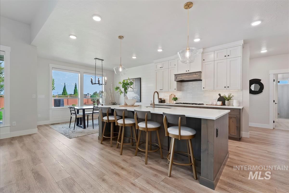 Kitchen with decorative light fixtures, a kitchen breakfast bar, white cabinets, backsplash, and a center island with sink