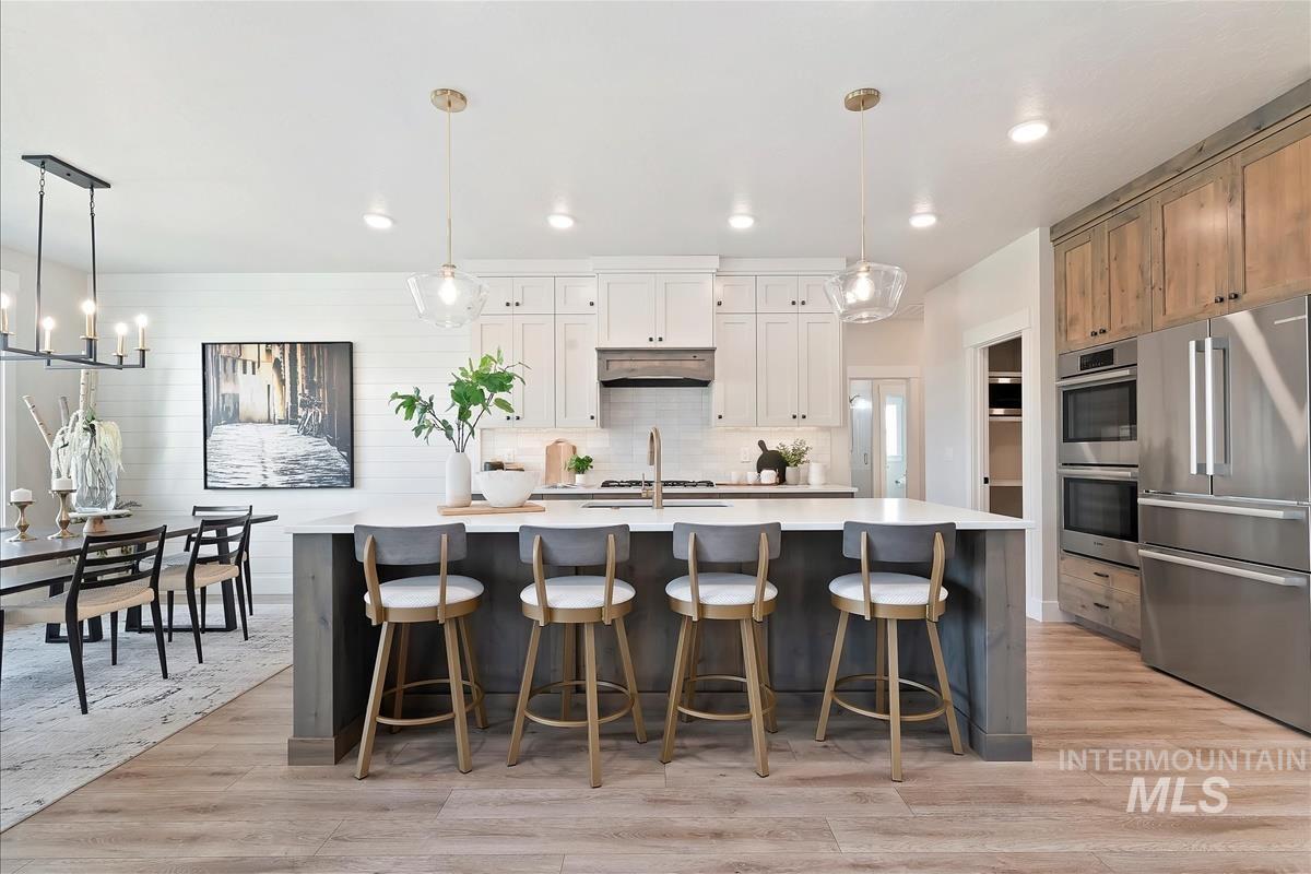 Kitchen featuring decorative light fixtures, appliances with stainless steel finishes, recessed lighting, light wood-style floors, and a center island with sink