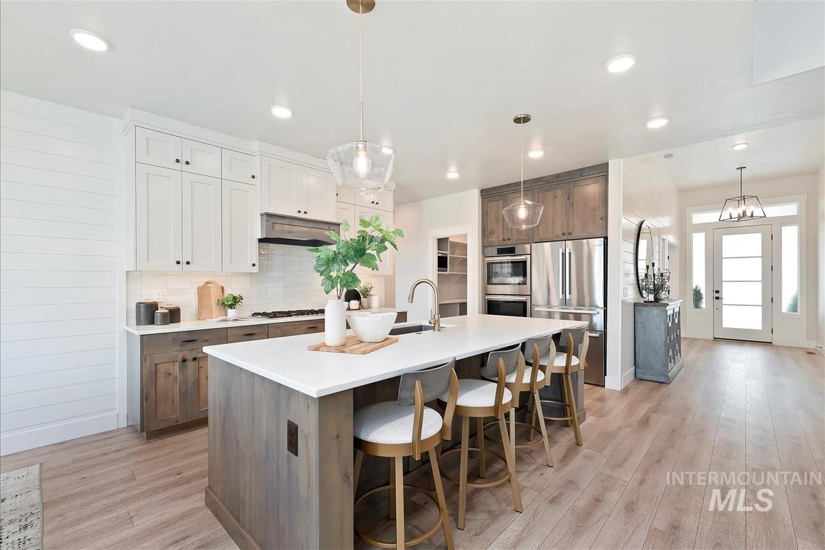 Kitchen with decorative backsplash, pendant lighting, appliances with stainless steel finishes, light wood-style flooring, and recessed lighting