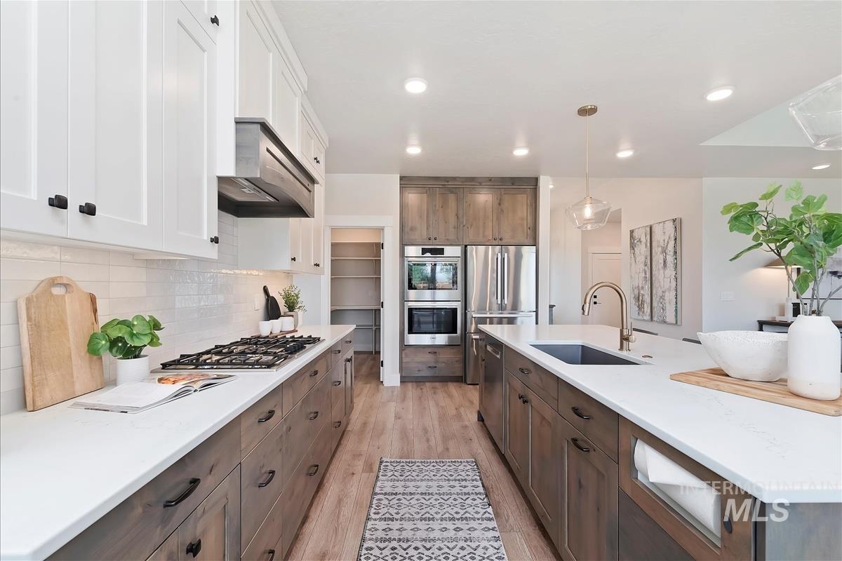 Kitchen featuring light wood-type flooring, decorative light fixtures, backsplash, a center island with sink, and appliances with stainless steel finishes