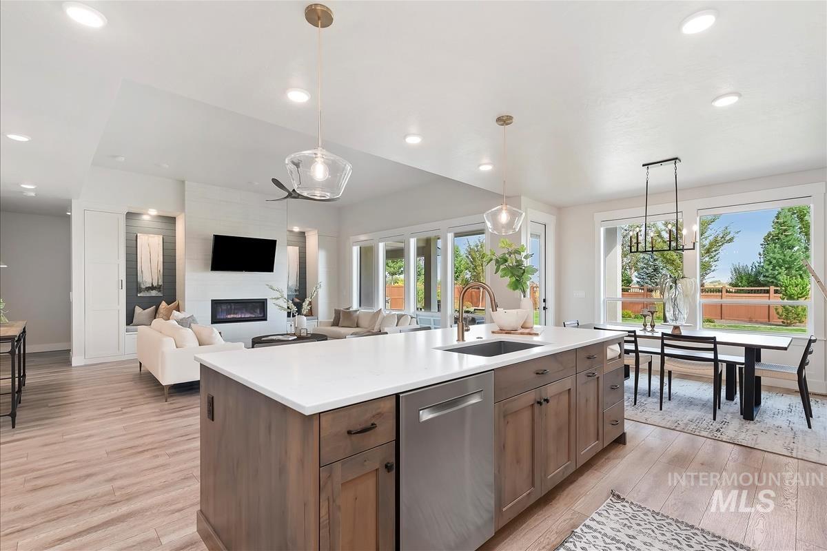 Kitchen with stainless steel dishwasher, light wood-type flooring, hanging light fixtures, brown cabinets, and recessed lighting
