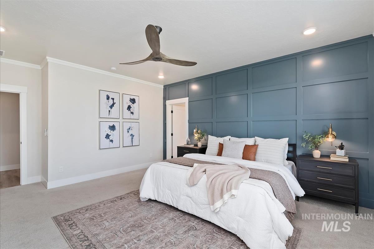 Bedroom with light colored carpet, a decorative wall, crown molding, and a ceiling fan