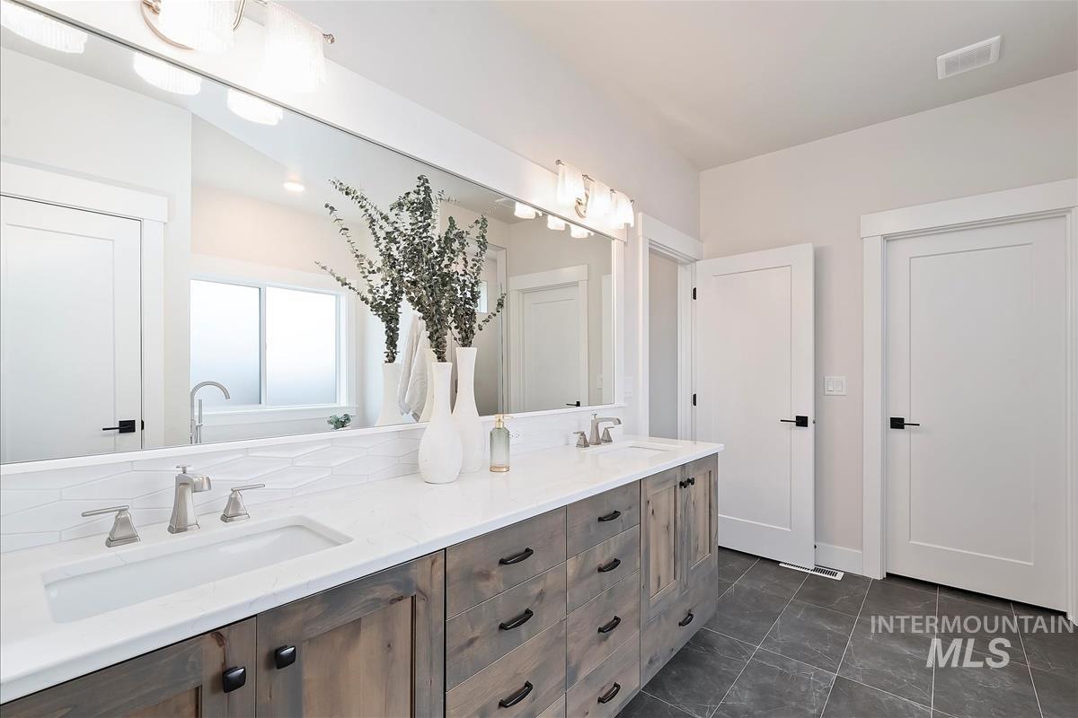 Full bath featuring double vanity and dark tile patterned flooring