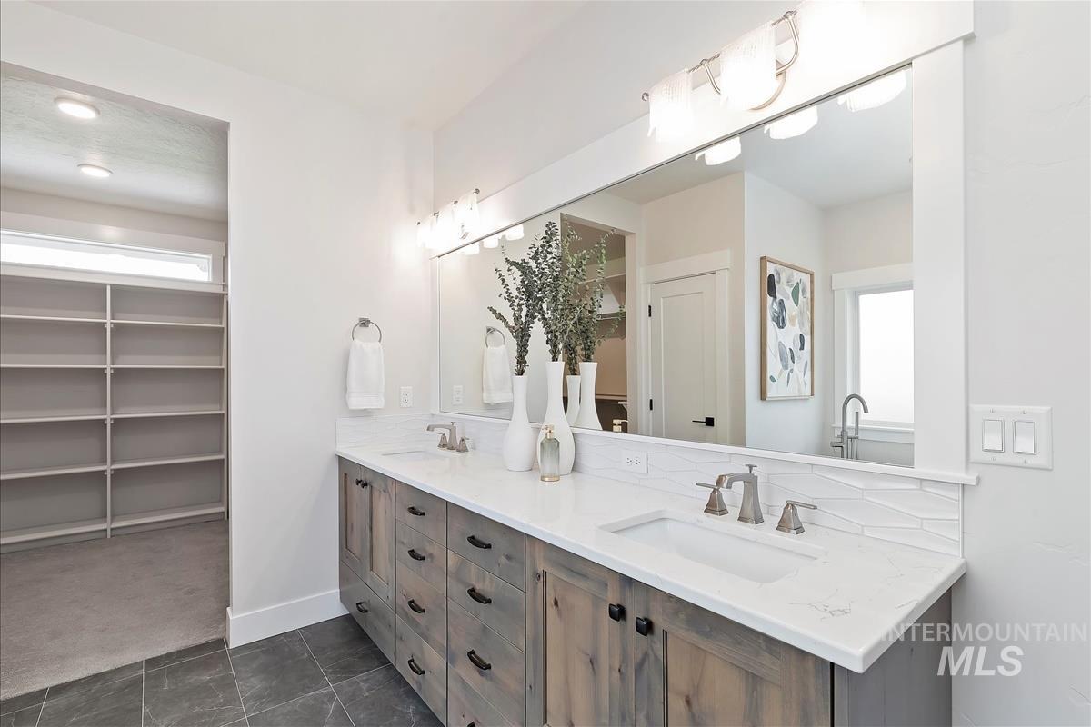 Bathroom with double vanity, a spacious closet, and dark tile patterned floors