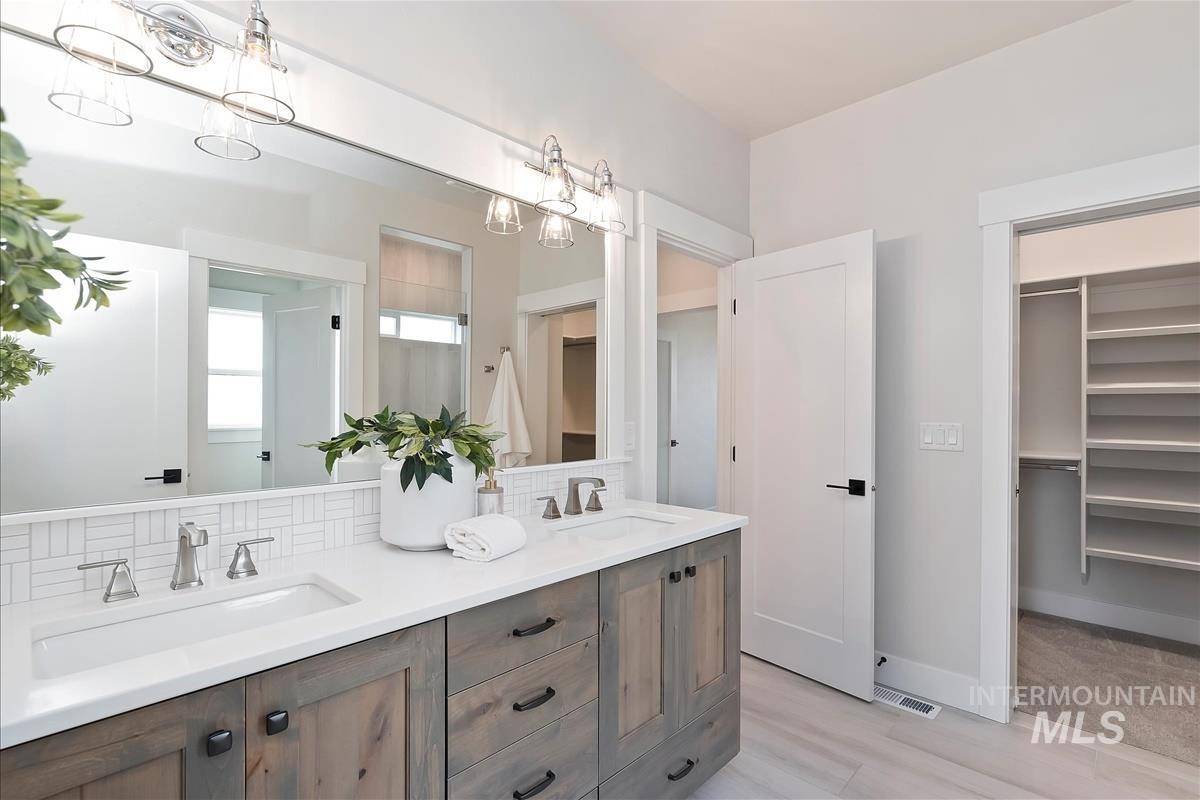 Bathroom featuring double vanity, tasteful backsplash, a spacious closet, a shower, and light wood-style flooring