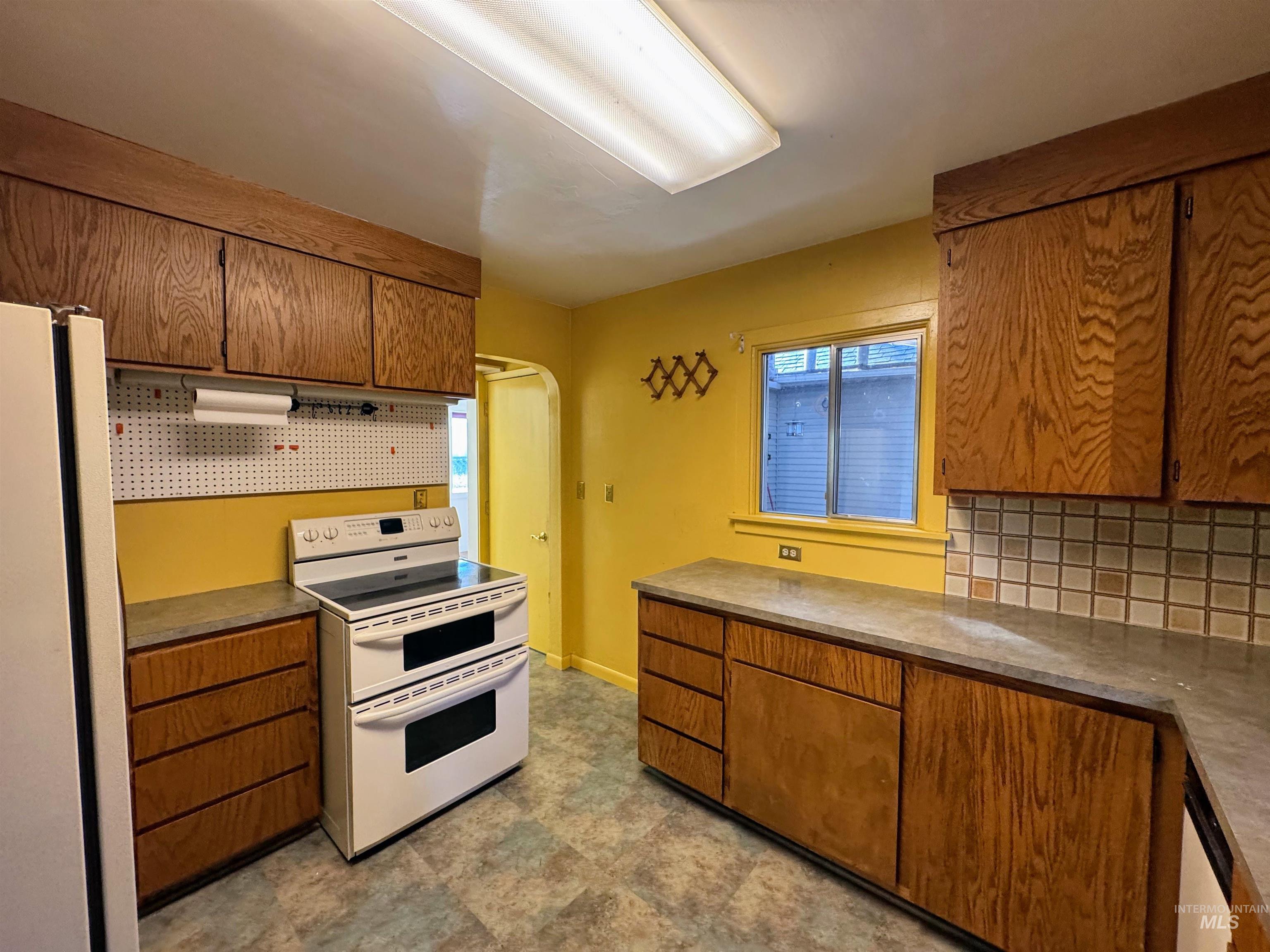 Kitchen featuring tasteful backsplash, white appliances, brown cabinetry, and arched walkways