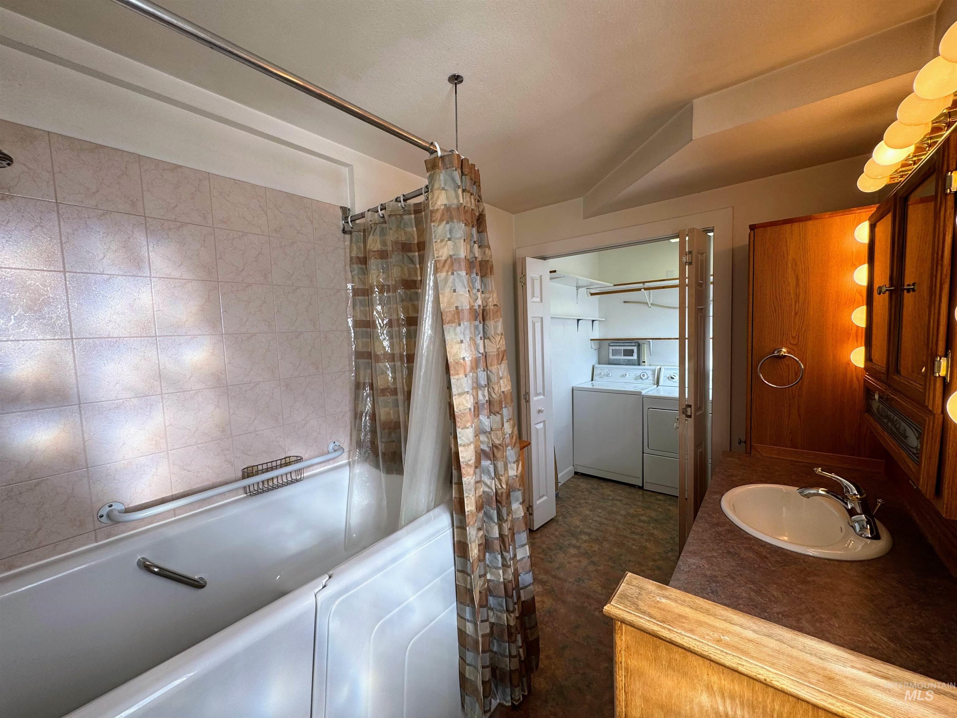 Bathroom featuring shower / bath combo with shower curtain, washing machine and dryer, and vanity