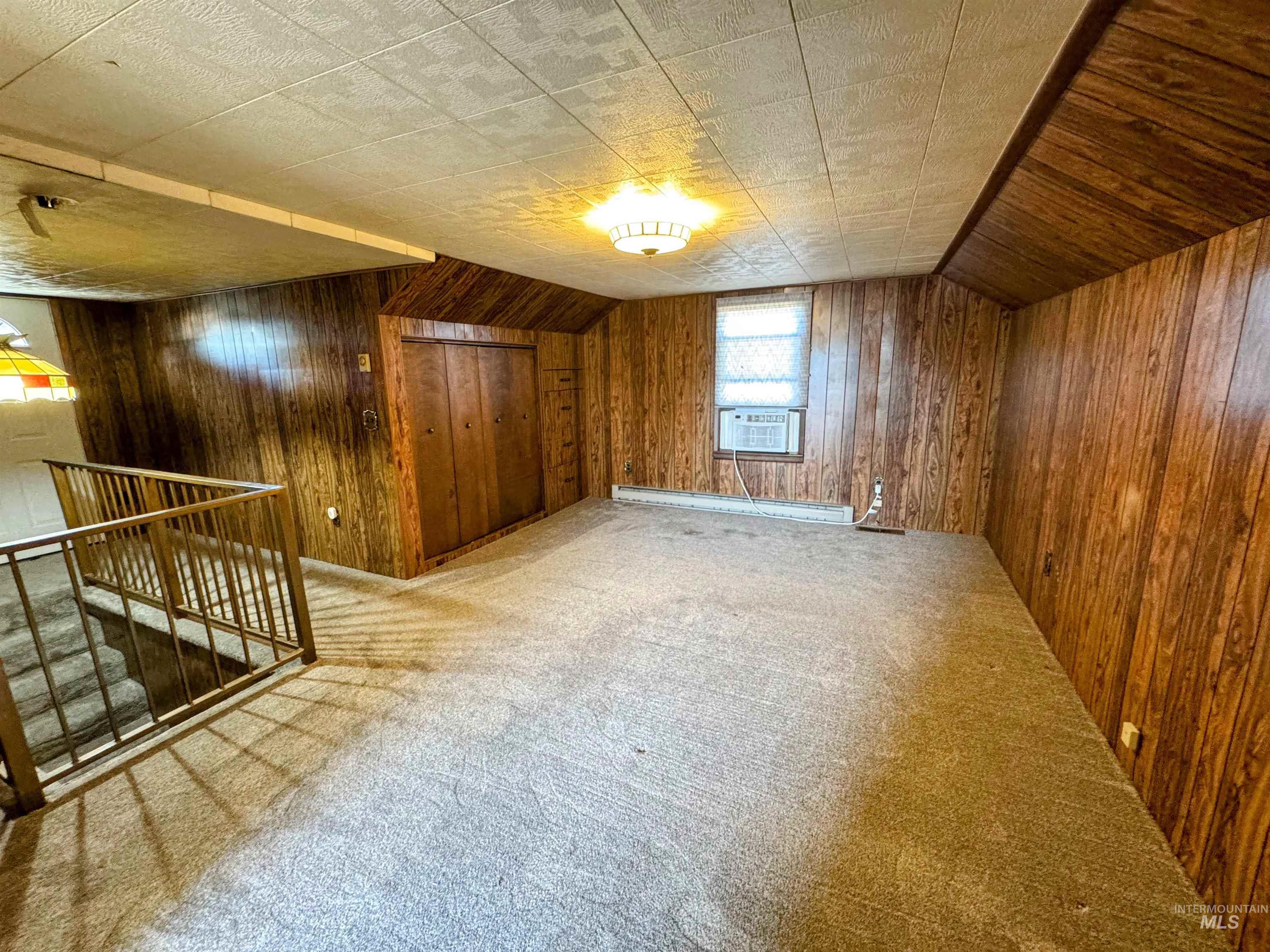 Bonus room featuring lofted ceiling, light colored carpet, wooden walls, and a baseboard heating unit