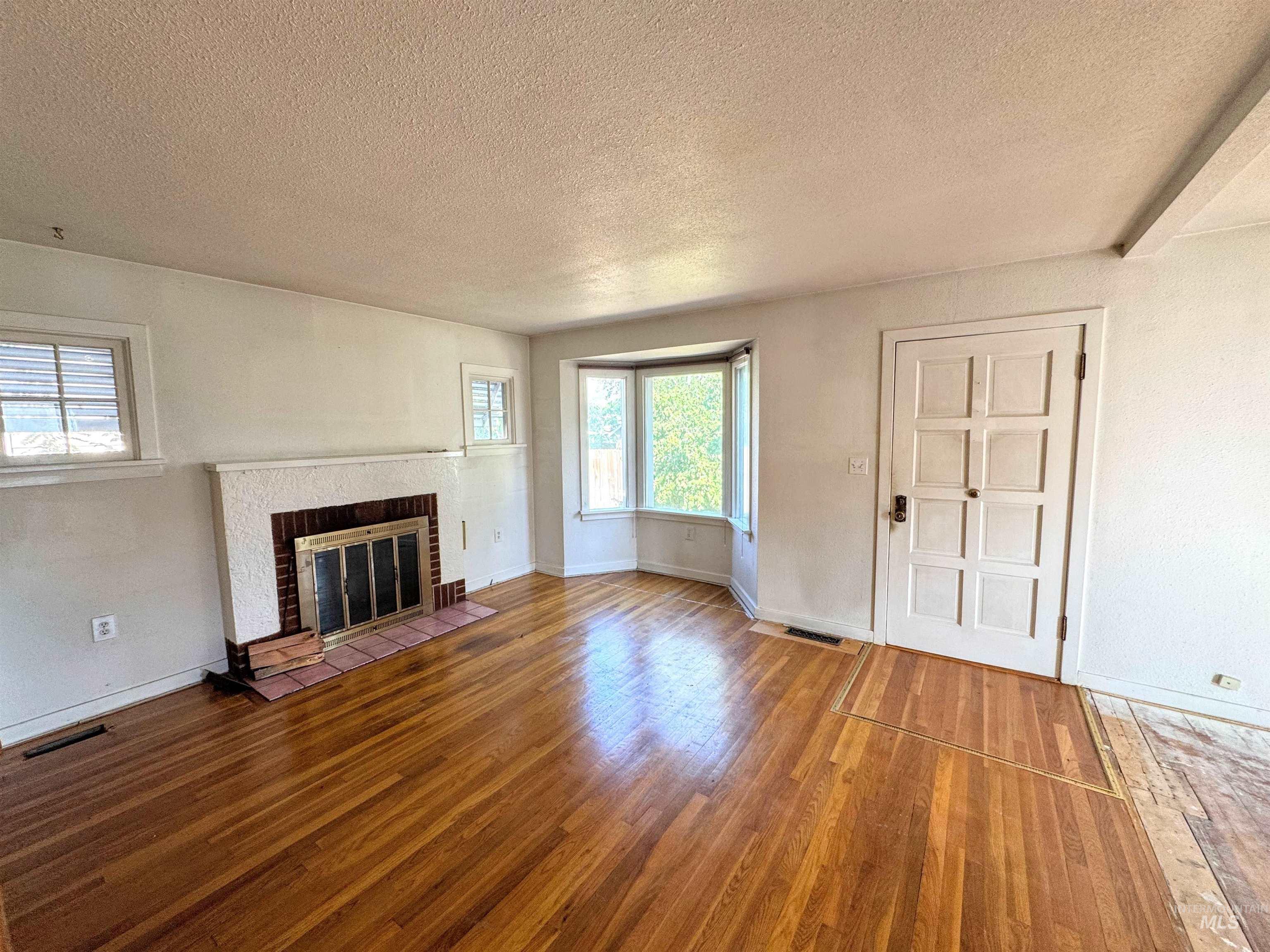 Unfurnished living room featuring wood finished floors, a brick fireplace, and a textured ceiling