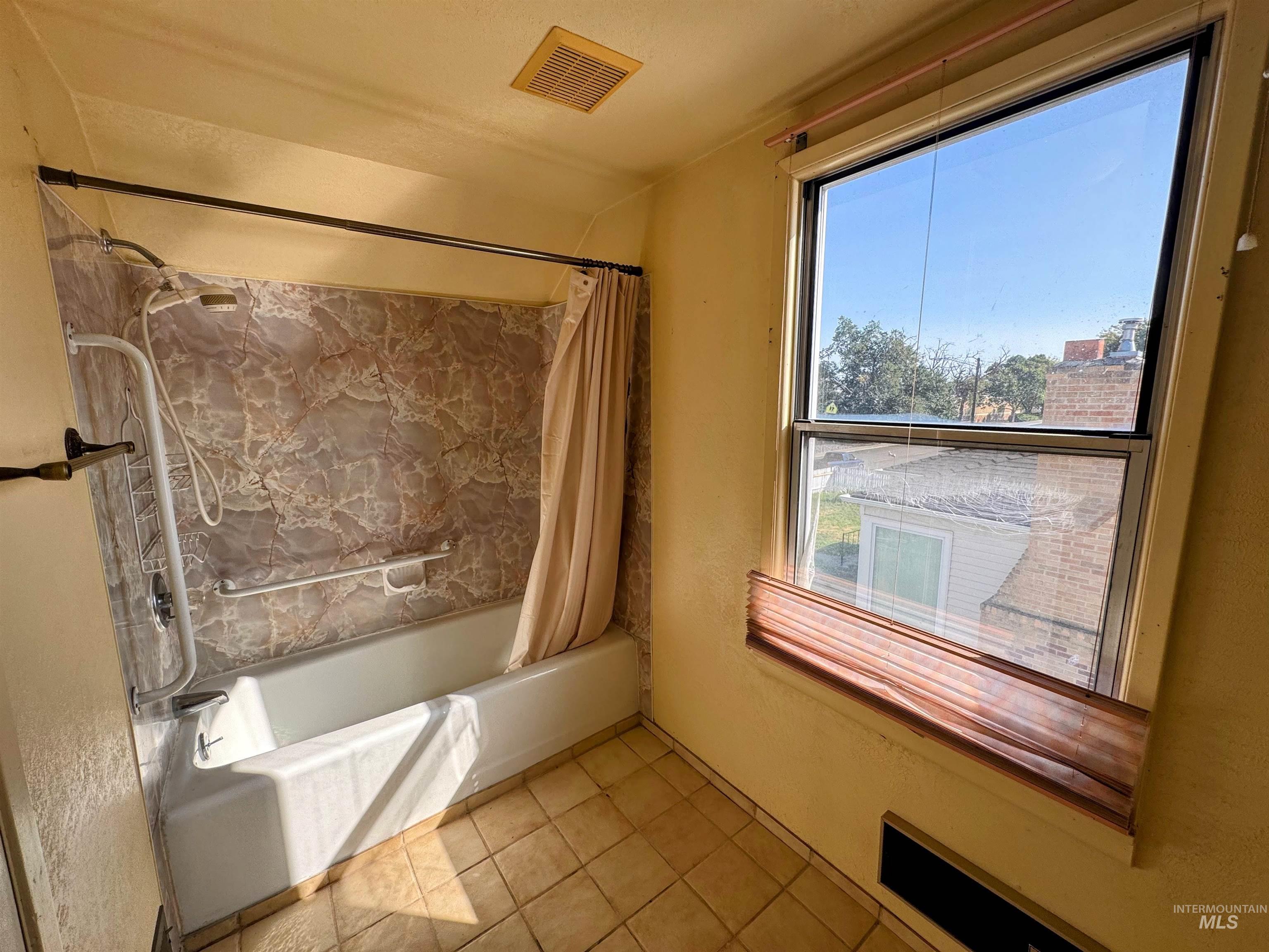 Full bathroom featuring shower / tub combo, light tile patterned floors, and a textured wall