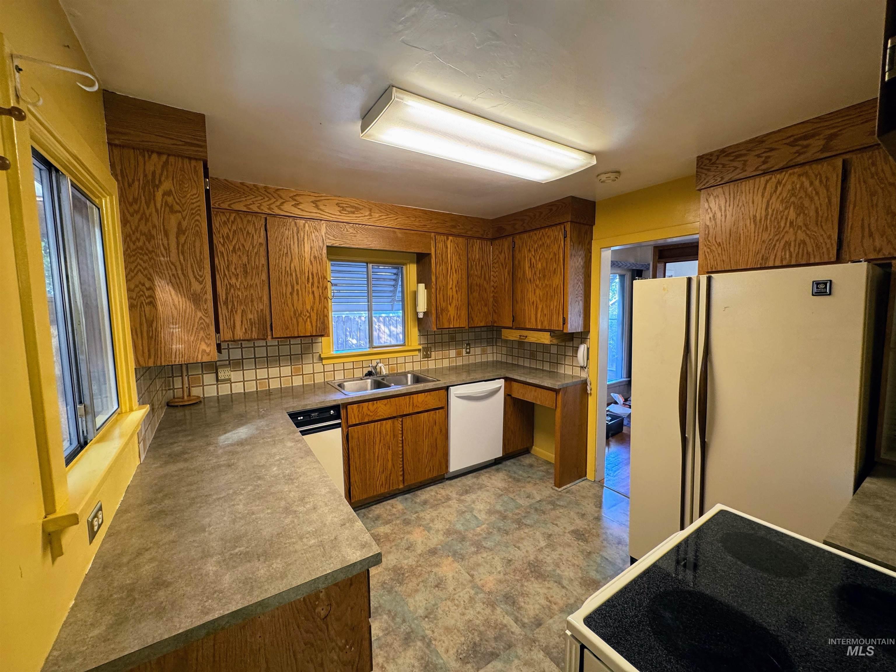 Kitchen with brown cabinets, decorative backsplash, white appliances, and dark countertops