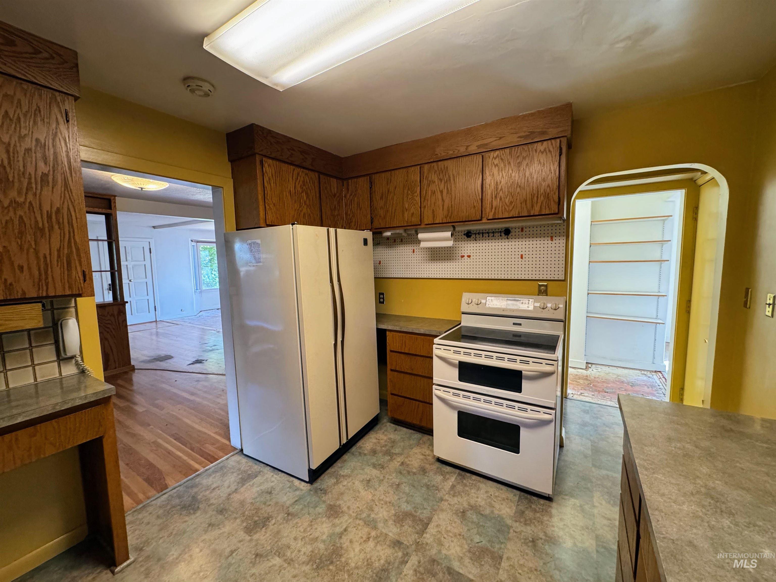 Kitchen with white appliances, brown cabinetry, backsplash, and light flooring