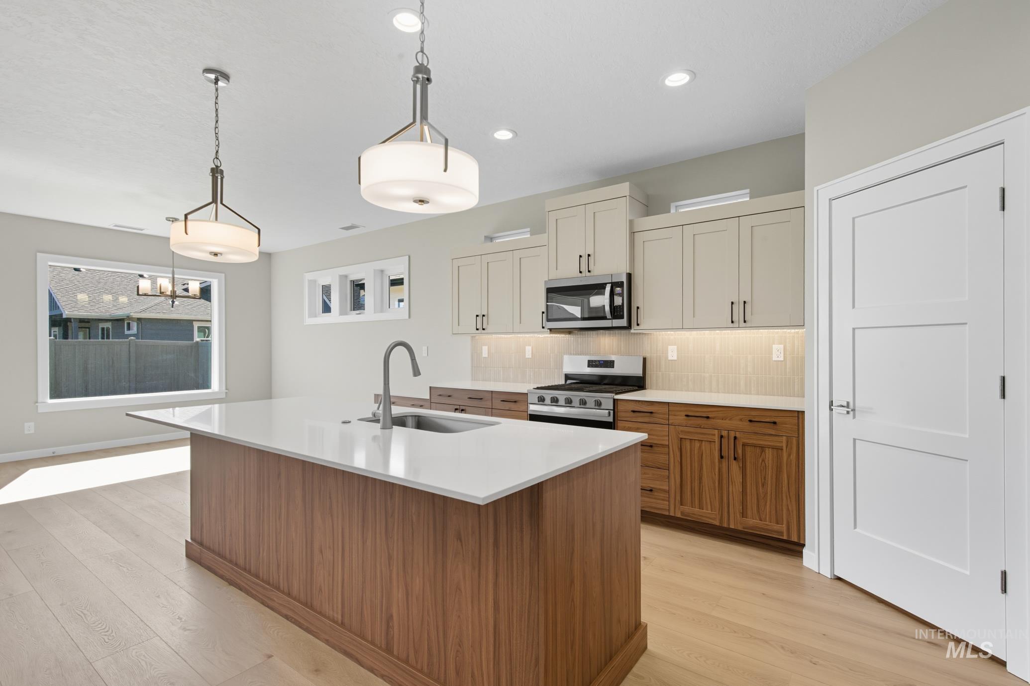 Kitchen with brown cabinets, decorative light fixtures, appliances with stainless steel finishes, tasteful backsplash, and a center island with sink