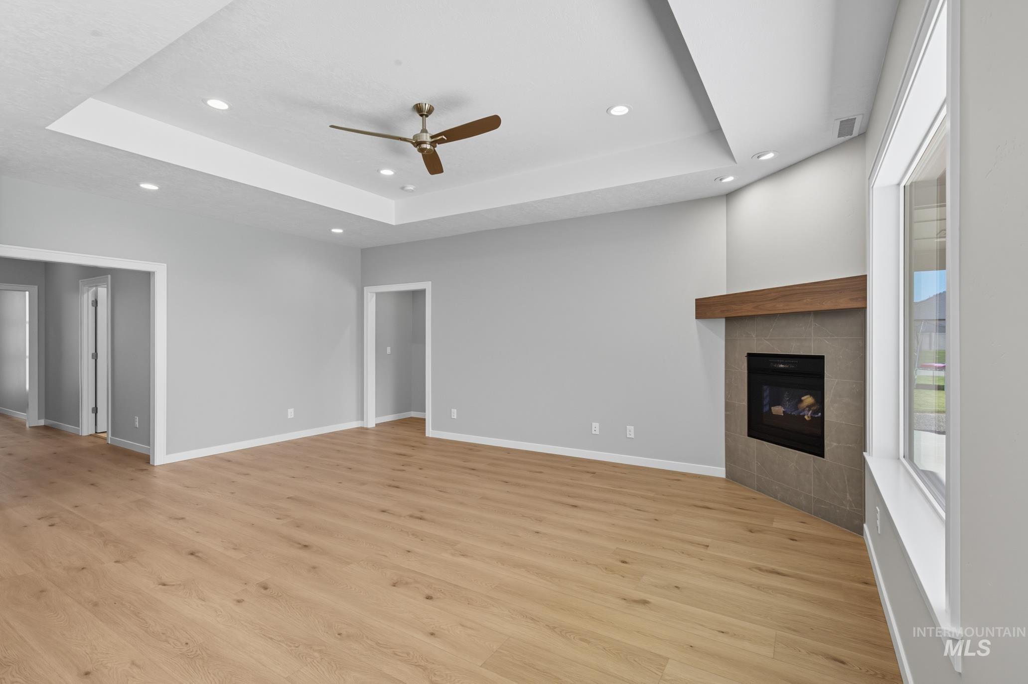 Unfurnished living room featuring a tray ceiling, a tile fireplace, light wood-style flooring, recessed lighting, and a ceiling fan