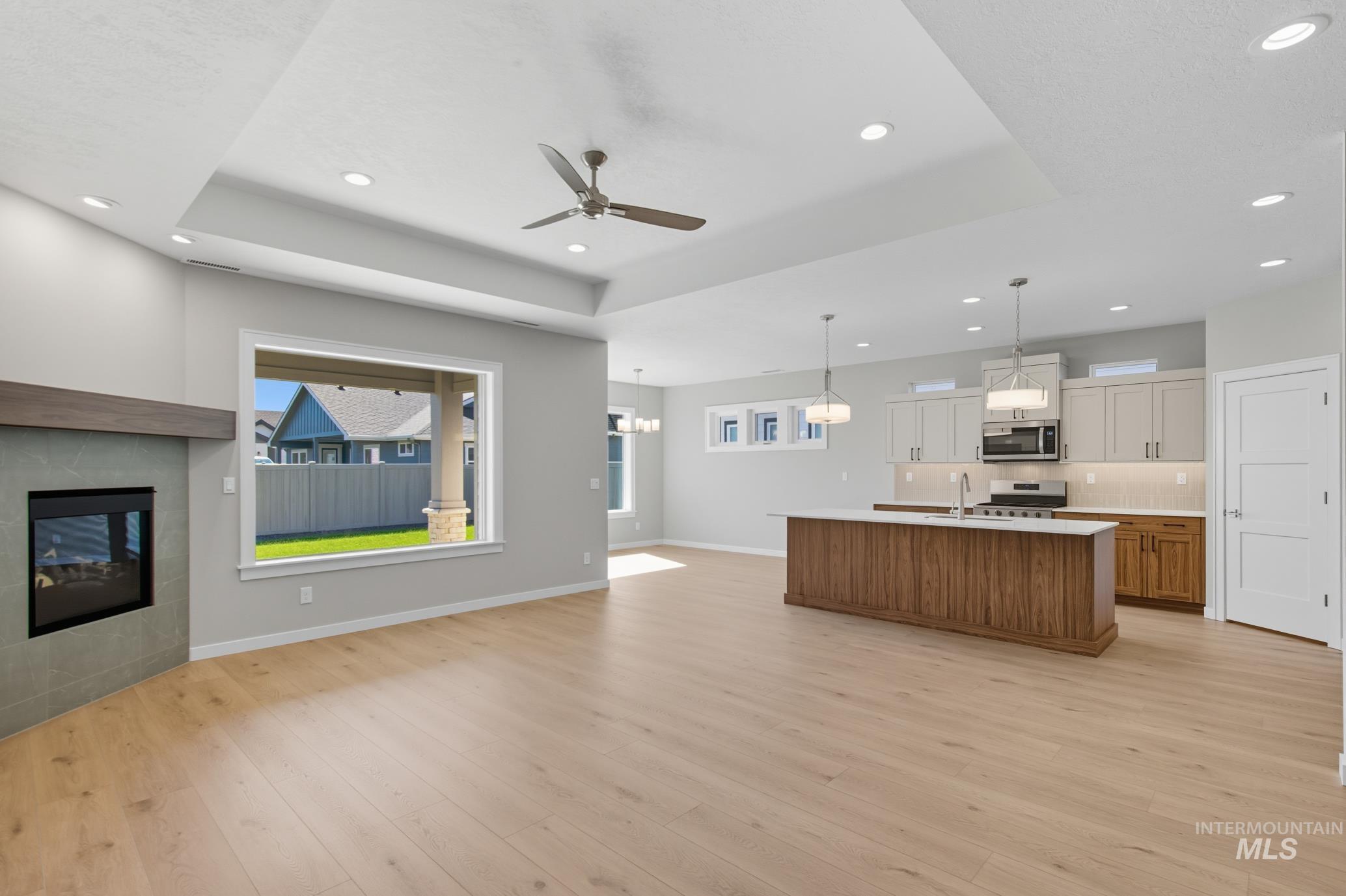 Kitchen with brown cabinetry, open floor plan, a raised ceiling, an island with sink, and recessed lighting