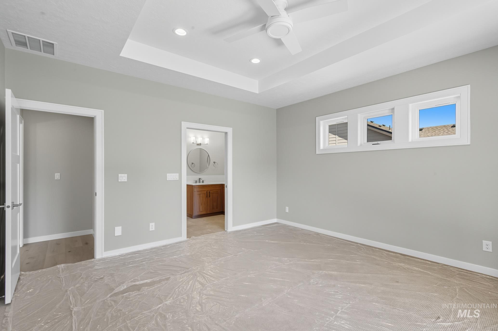 Unfurnished bedroom with a tray ceiling, ceiling fan, recessed lighting, and ensuite bathroom