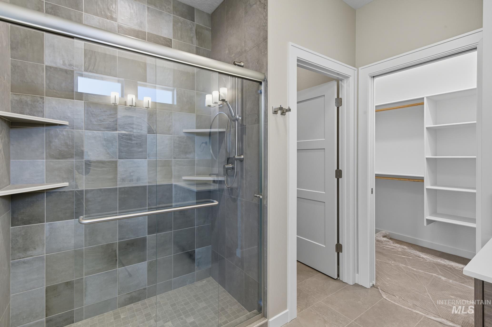 Full bath featuring a stall shower, a spacious closet, and light tile patterned floors