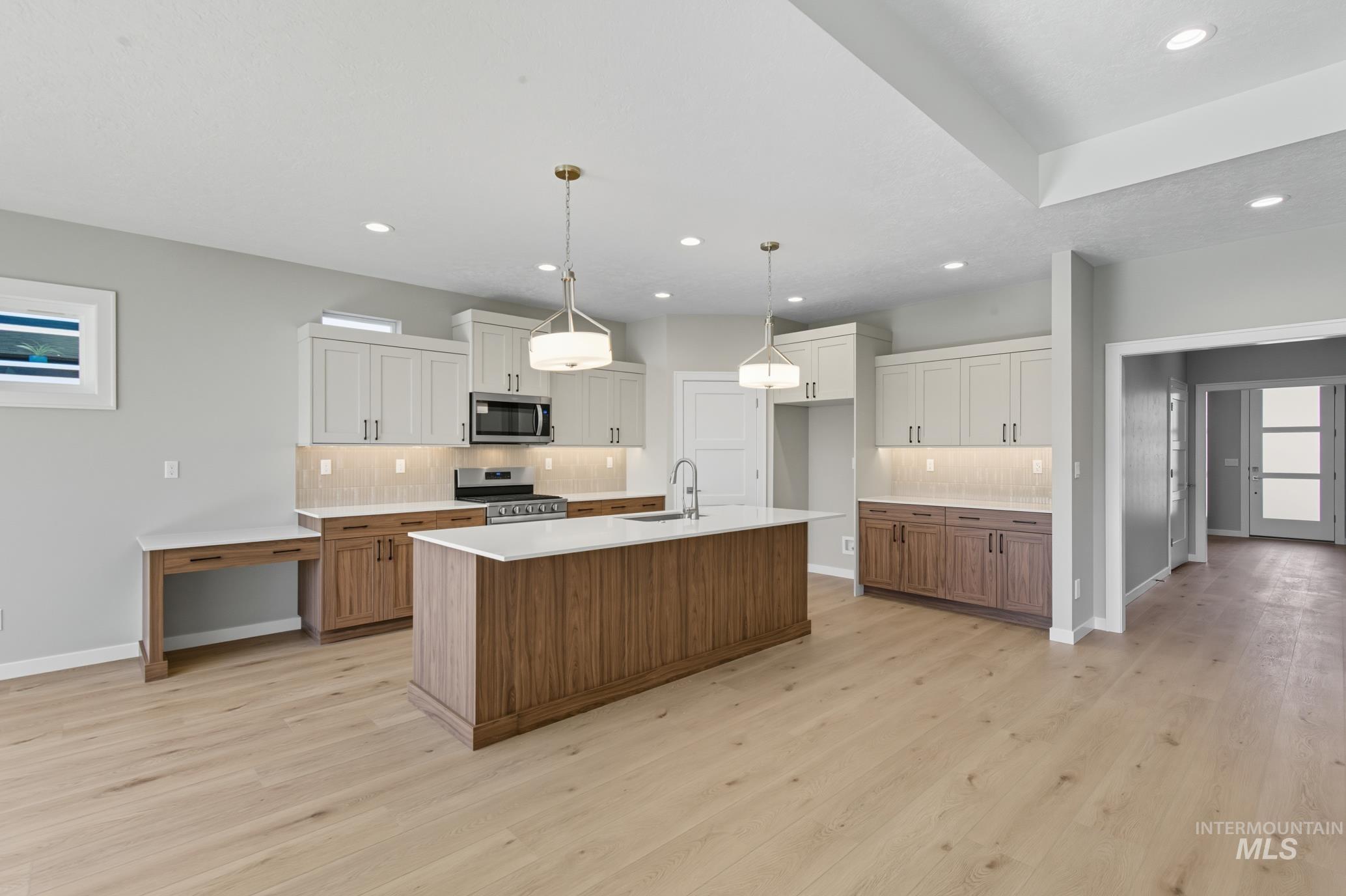 Kitchen with brown cabinetry, decorative backsplash, an island with sink, decorative light fixtures, and white cabinetry