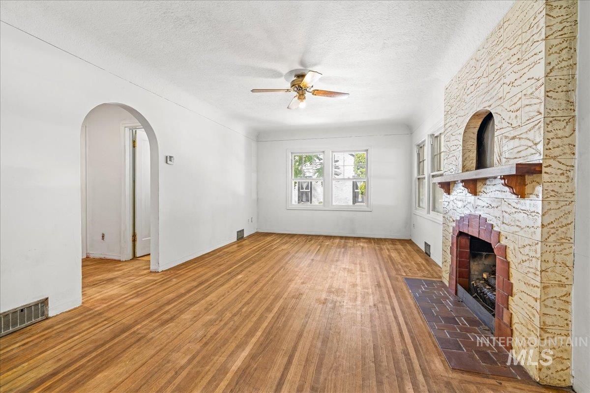 Unfurnished living room with arched walkways, wood finished floors, a textured ceiling, ceiling fan, and a stone fireplace