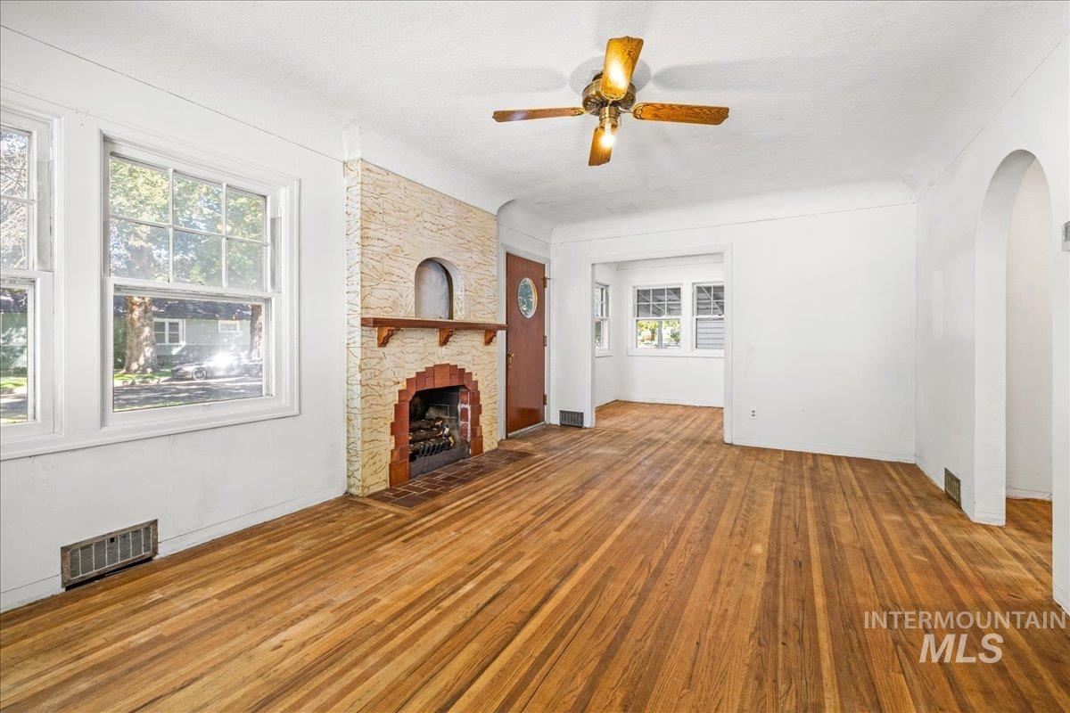 Unfurnished living room with ceiling fan, wood finished floors, a textured ceiling, a fireplace, and arched walkways