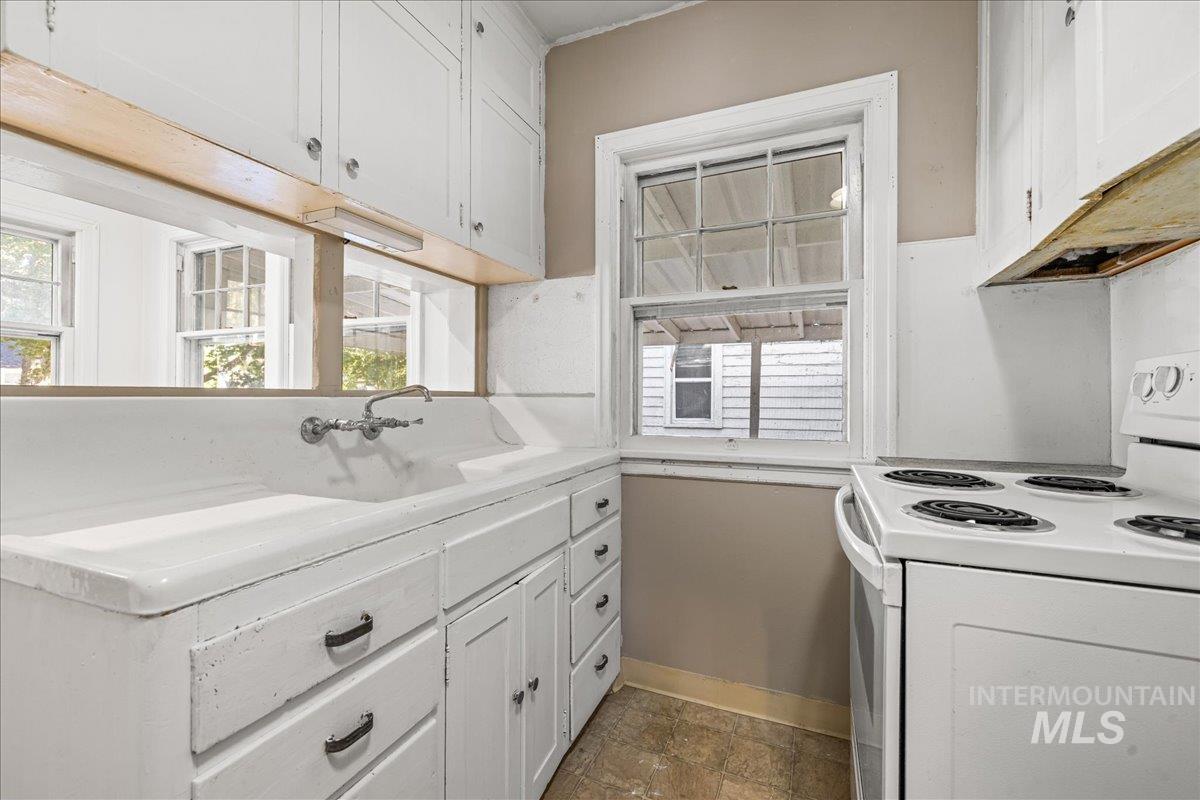 Kitchen with electric range, white cabinetry, light countertops, and dark stone finish flooring