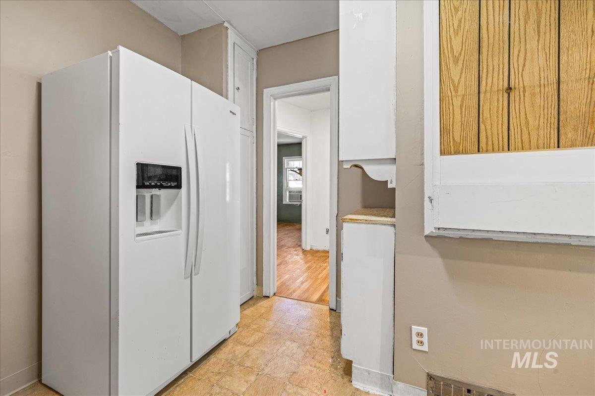 Kitchen featuring white fridge with ice dispenser, white cabinetry, and light countertops