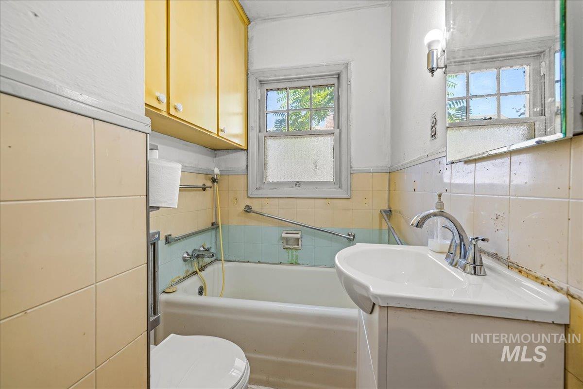 Full bath featuring vanity, a garden tub, and tile walls