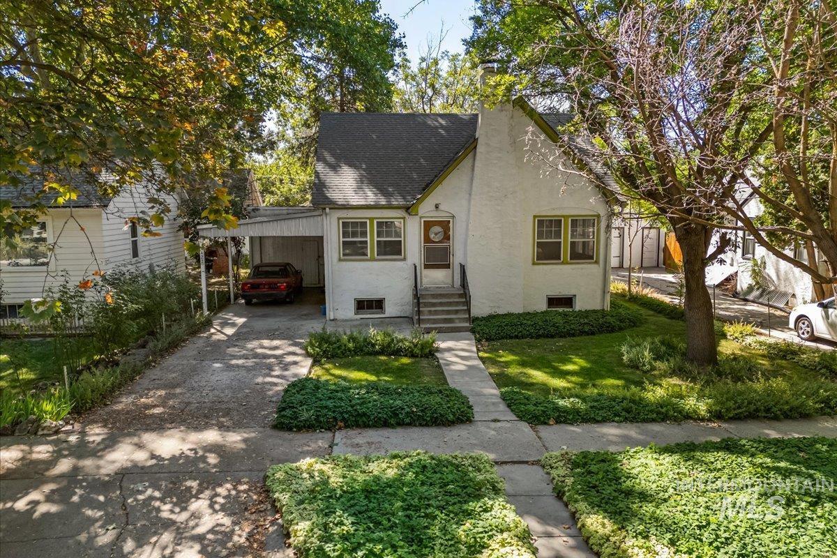 Tudor house with stucco siding, roof with shingles, a chimney, a carport, and driveway