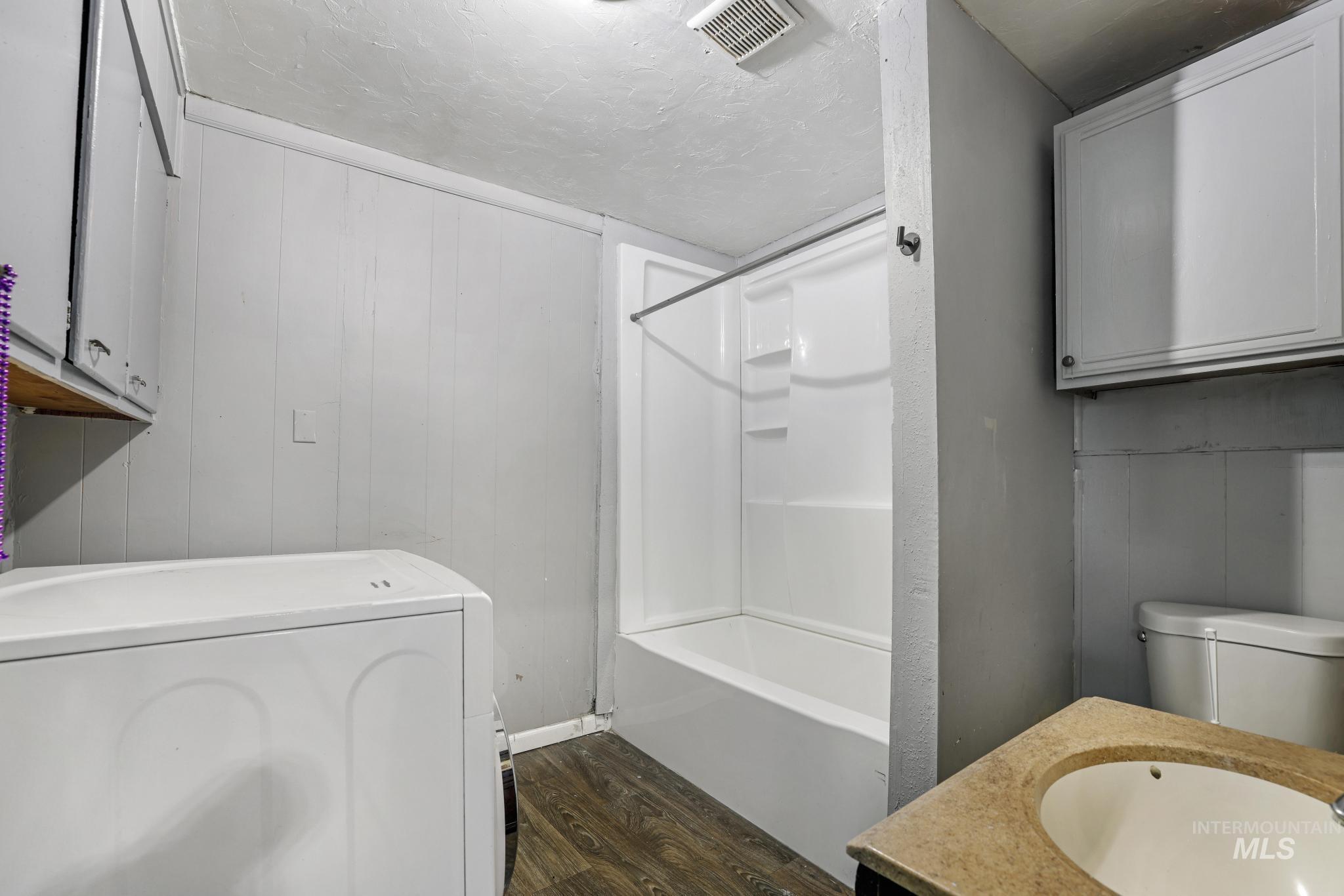 Bathroom featuring wood walls, washer / dryer, dark wood-type flooring, a textured ceiling, and shower / washtub combination