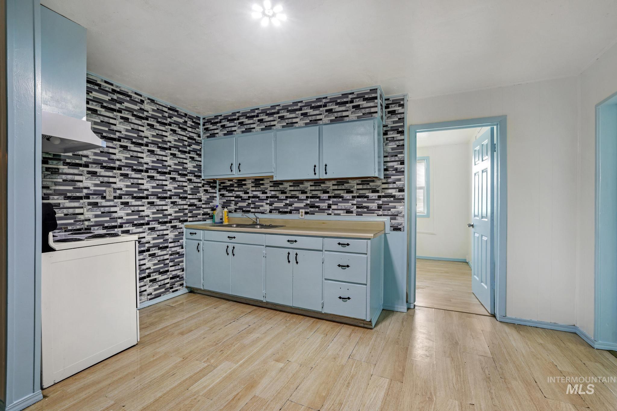 Kitchen featuring electric stove, light countertops, light wood-style floors, island range hood, and decorative backsplash