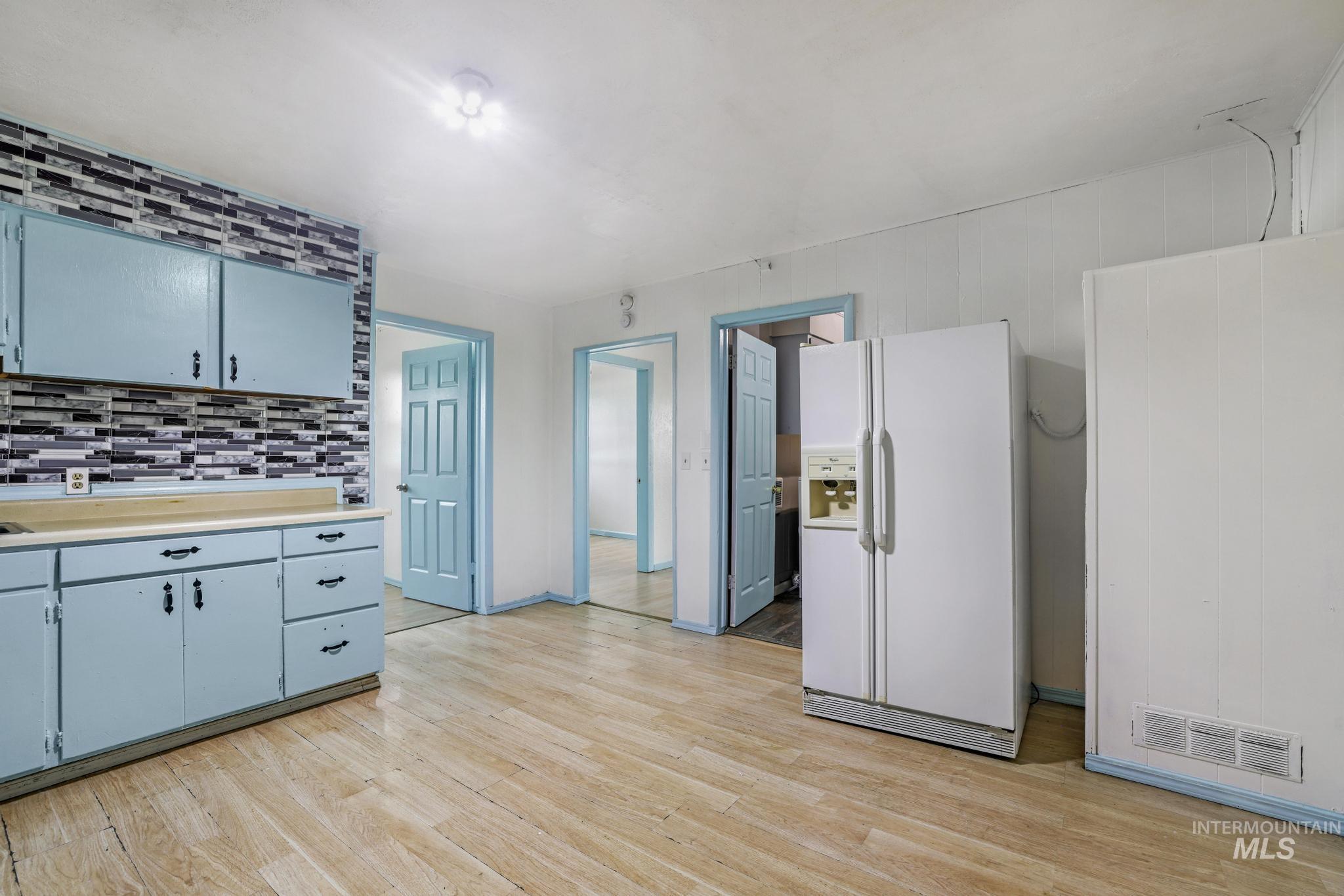 Kitchen with white refrigerator with ice dispenser, light countertops, light wood-style floors, and tasteful backsplash