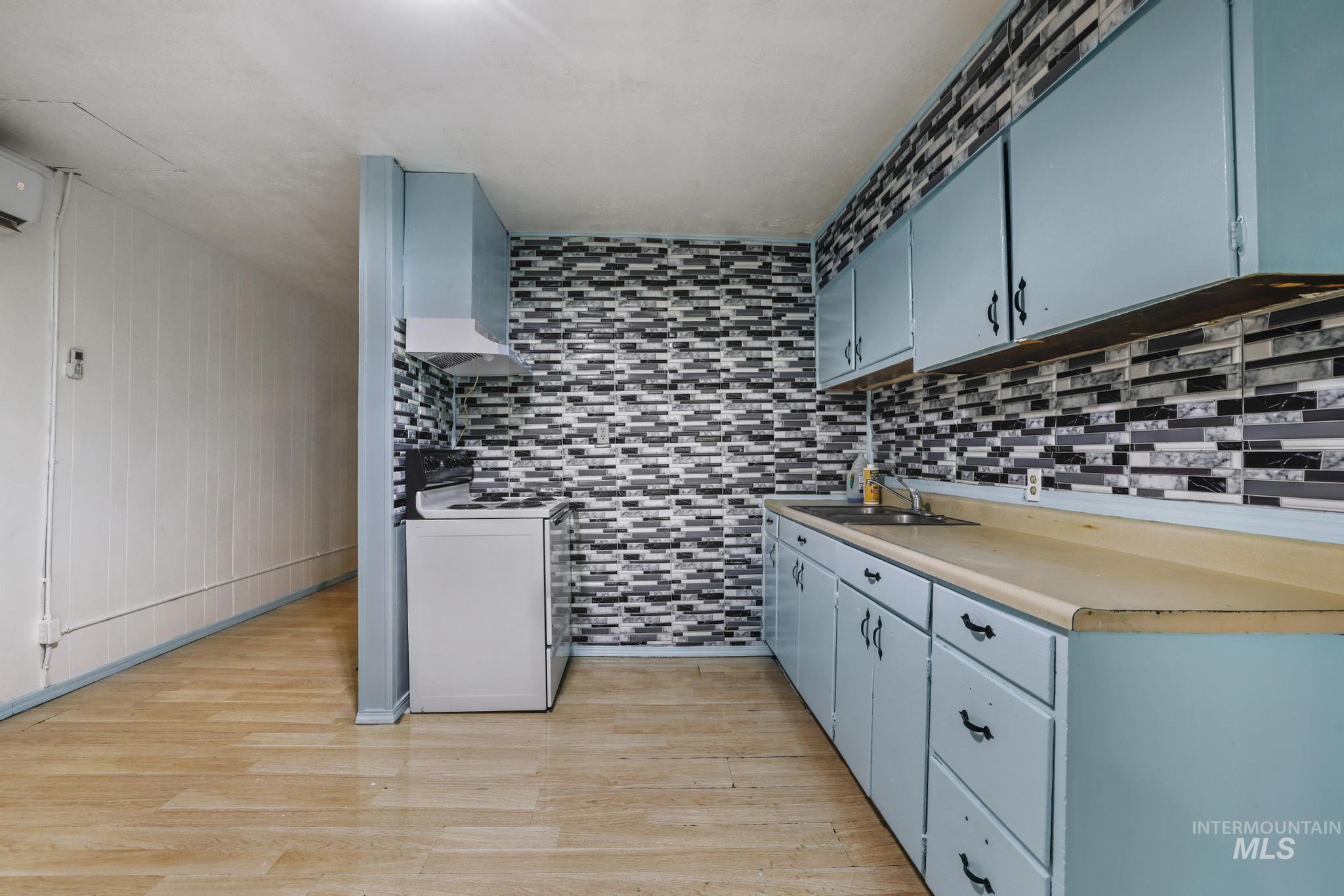 Kitchen with blue cabinetry, white electric stove, light countertops, light wood-style flooring, and extractor fan