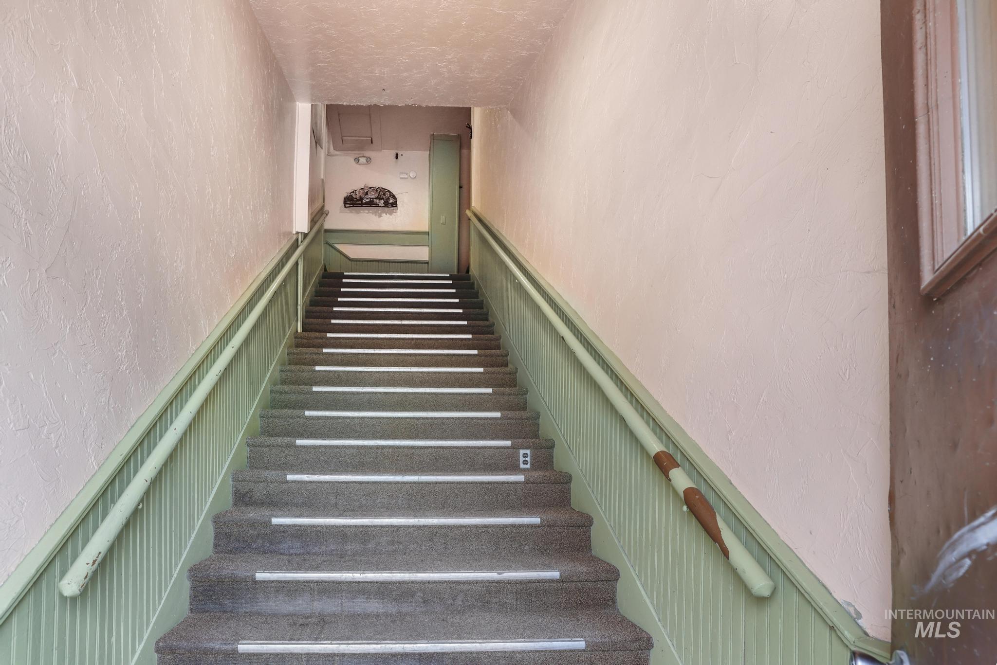 Stairway featuring a textured wall, wainscoting, a decorative wall, attic access, and a textured ceiling