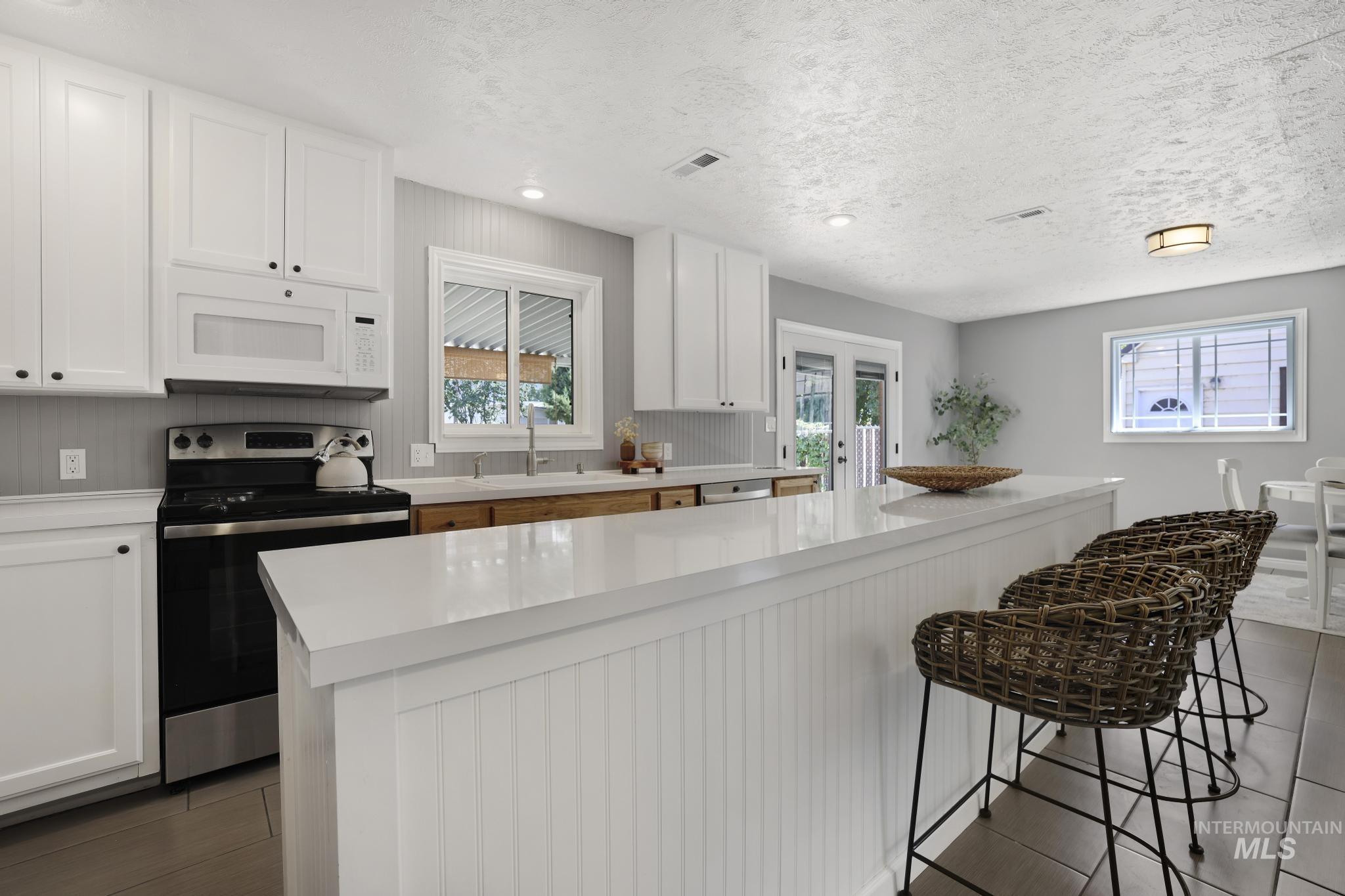 Kitchen with white cabinets, stainless steel electric range, white microwave, healthy amount of natural light, and recessed lighting