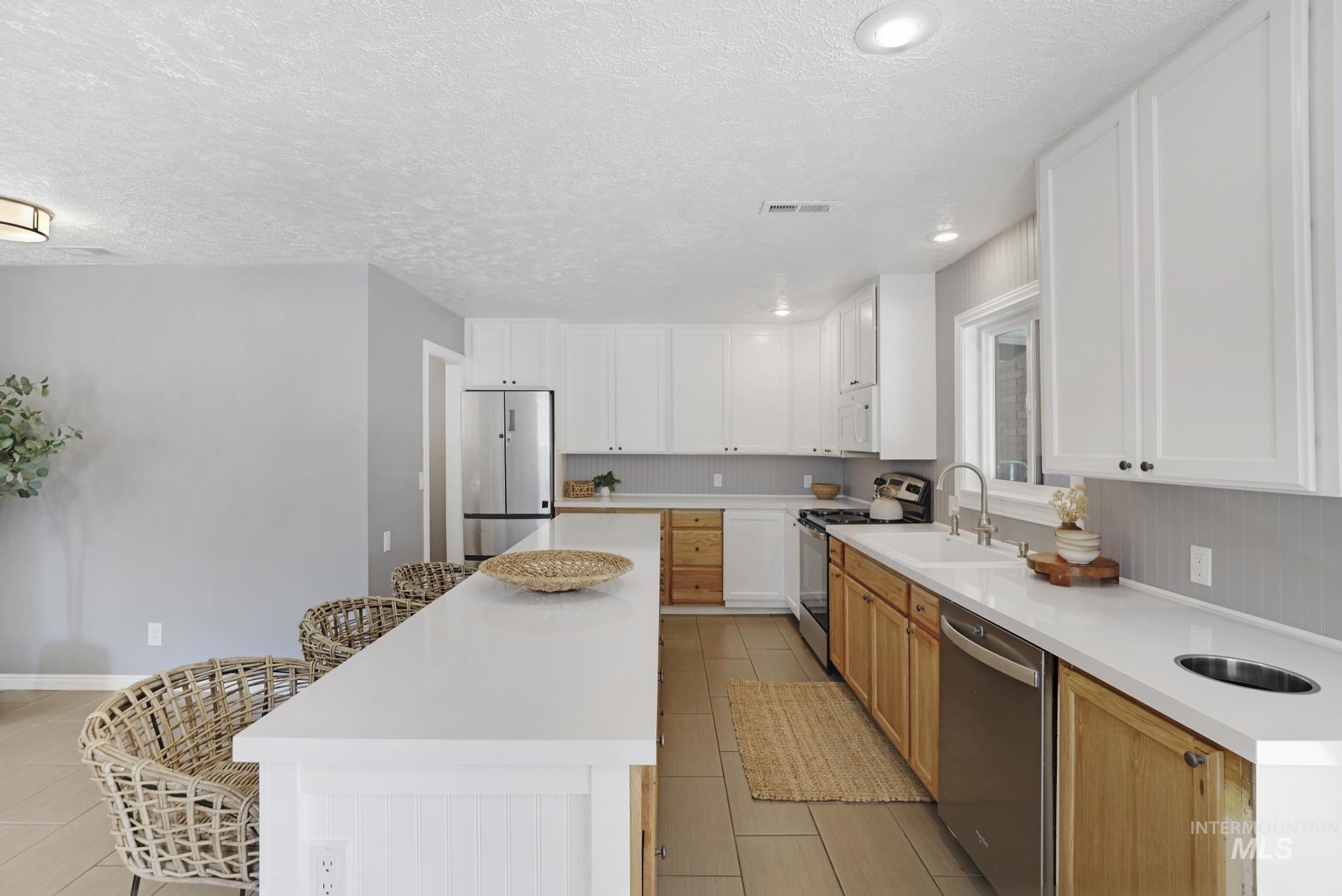 Kitchen featuring a textured ceiling, white cabinetry, stainless steel appliances, light stone counters, and a breakfast bar