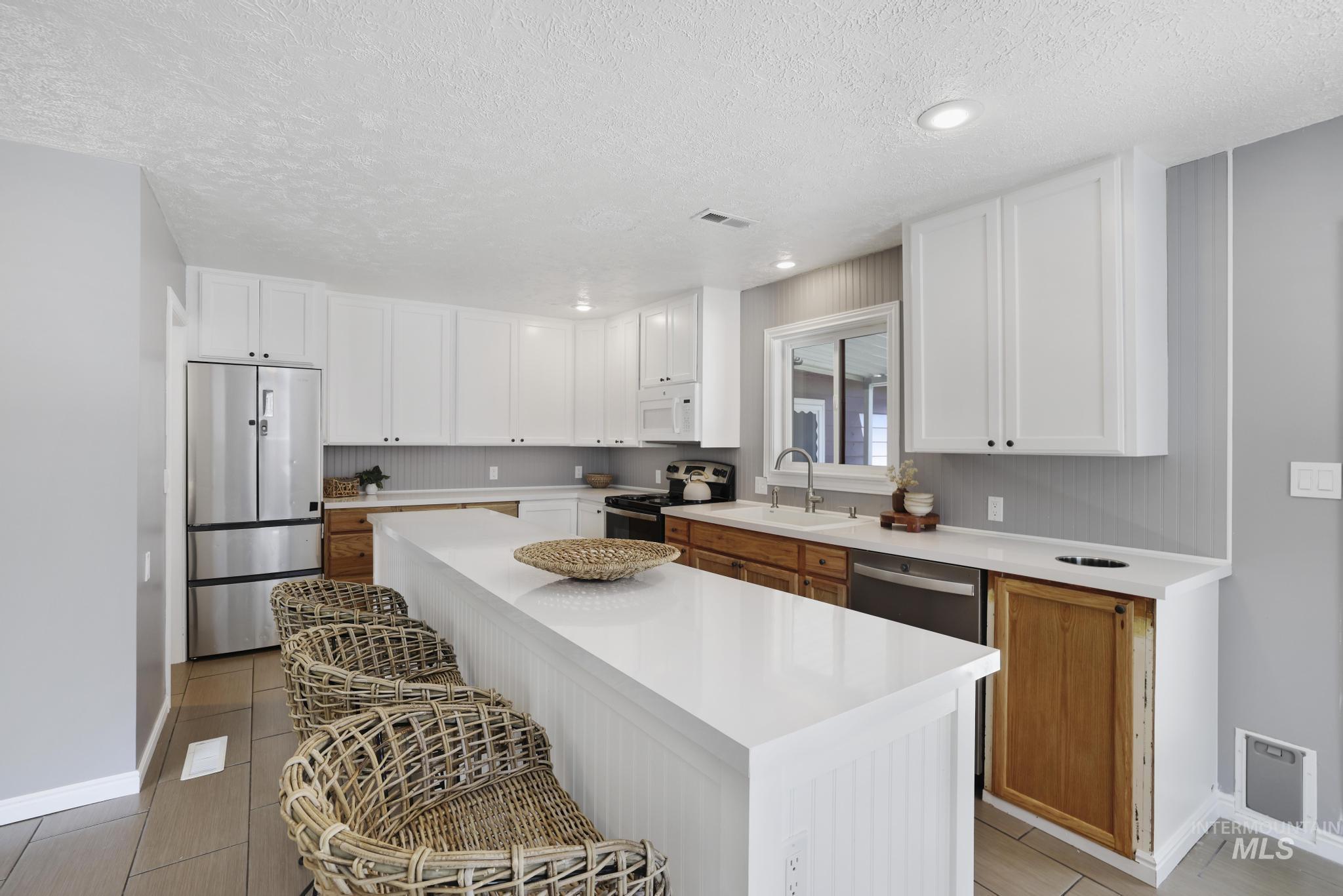 Kitchen with white cabinets, a breakfast bar, stainless steel appliances, a textured ceiling, and a center island