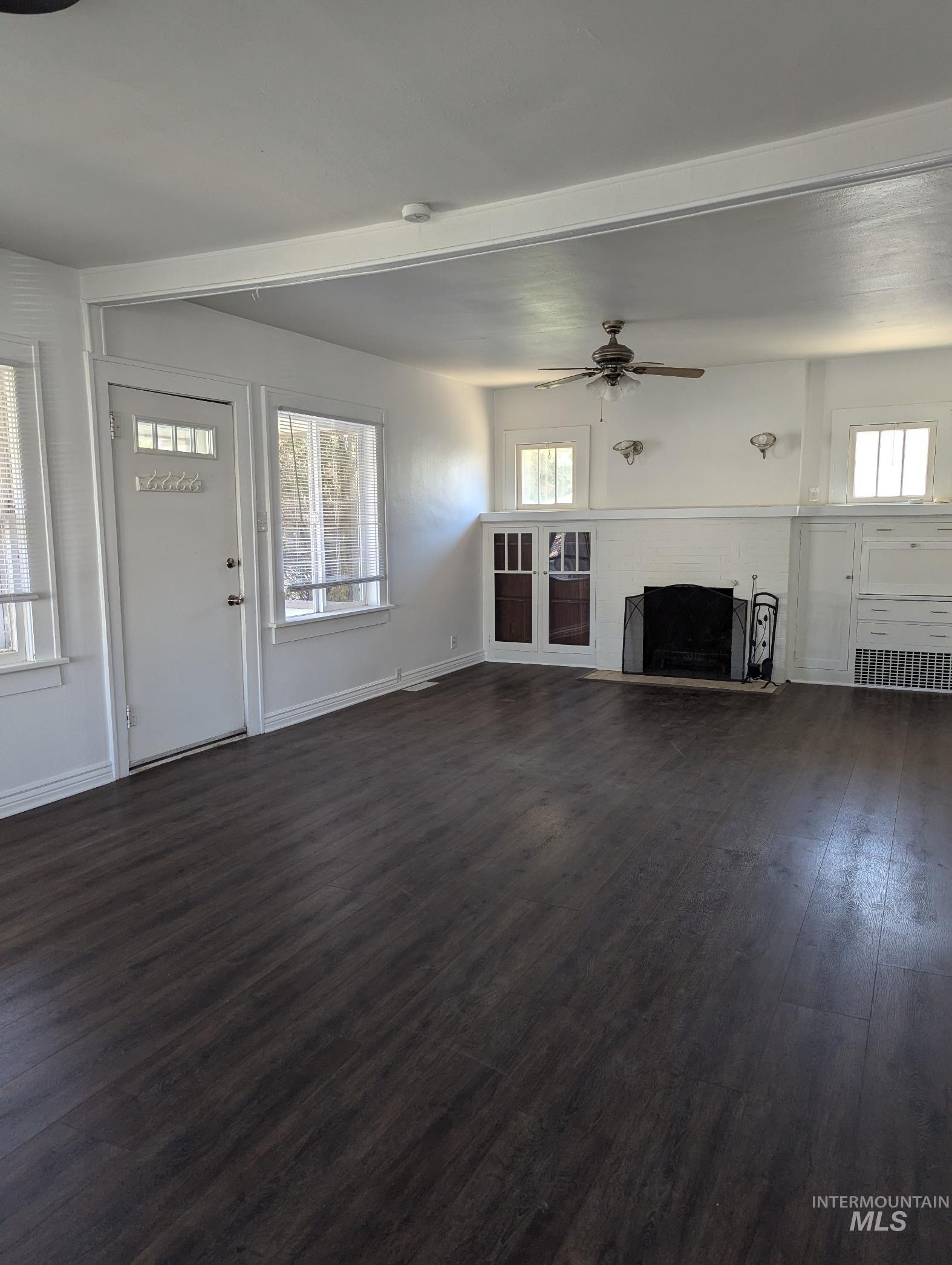 Unfurnished living room featuring dark wood-style flooring, ceiling fan, and a fireplace with raised hearth