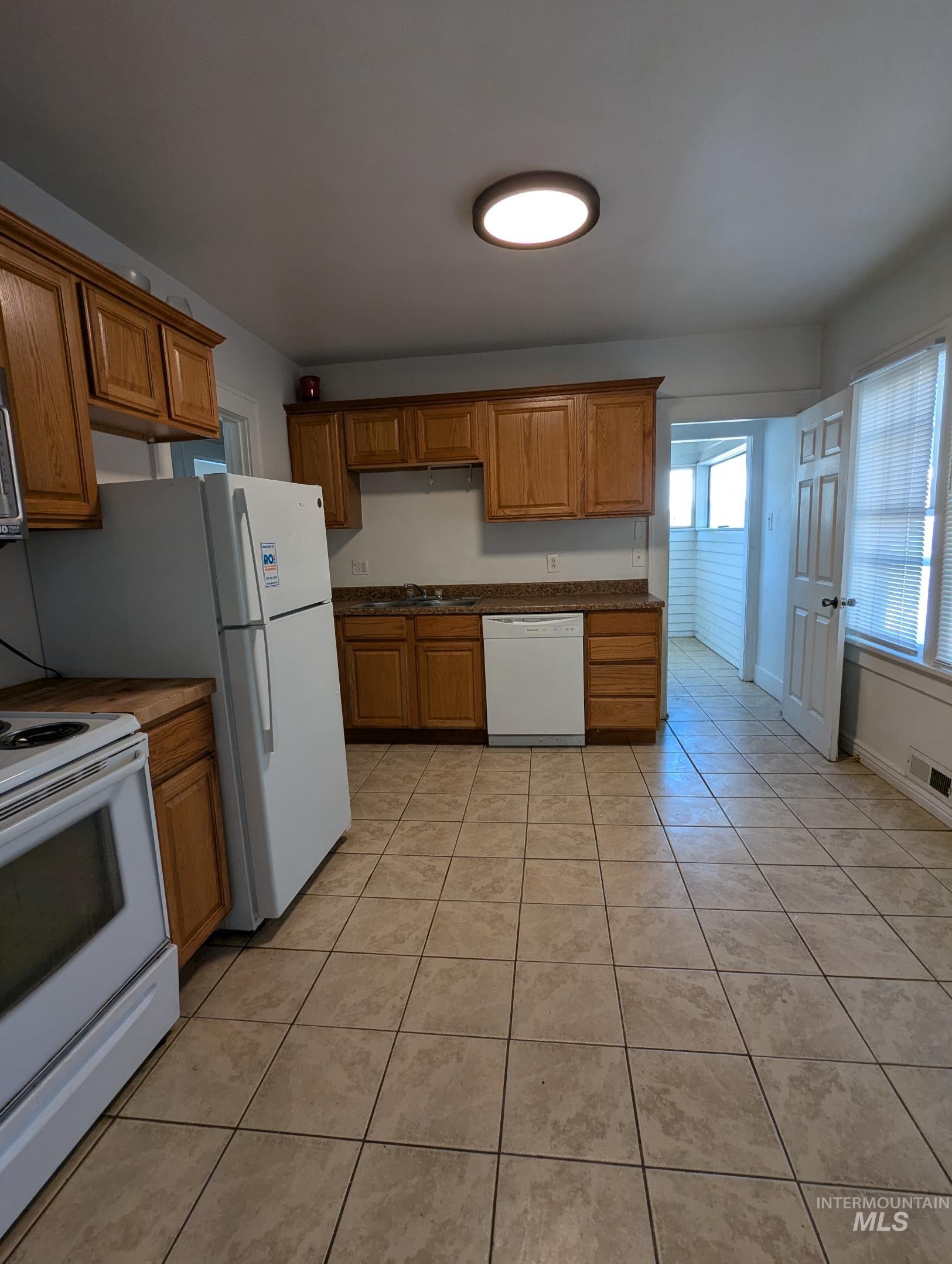 Kitchen featuring white appliances, light tile patterned flooring, and brown cabinetry
