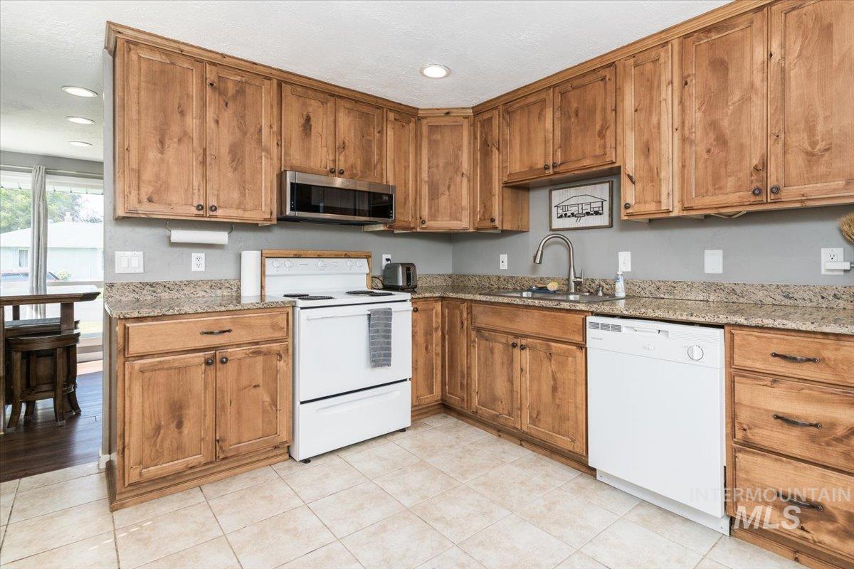 Kitchen with light stone counters, white appliances, brown cabinetry, light tile patterned floors, and recessed lighting