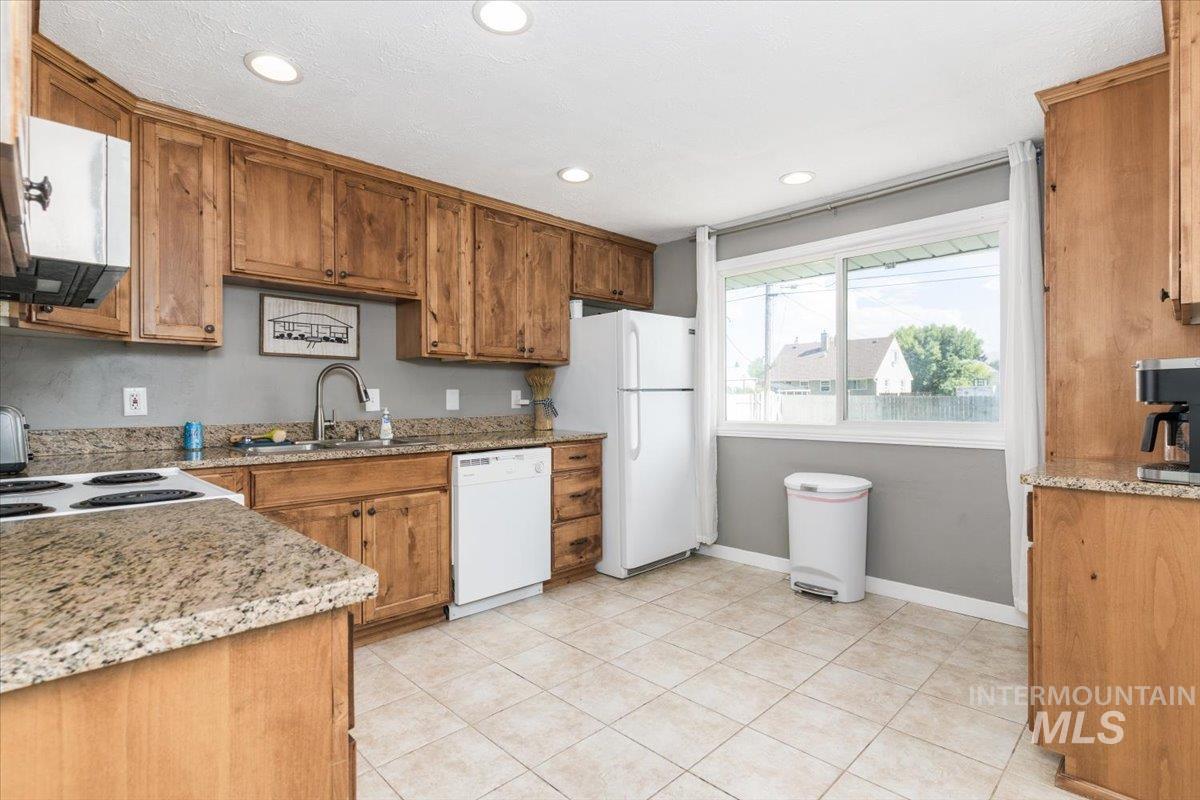 Kitchen featuring light stone counters, brown cabinets, white appliances, light tile patterned floors, and recessed lighting